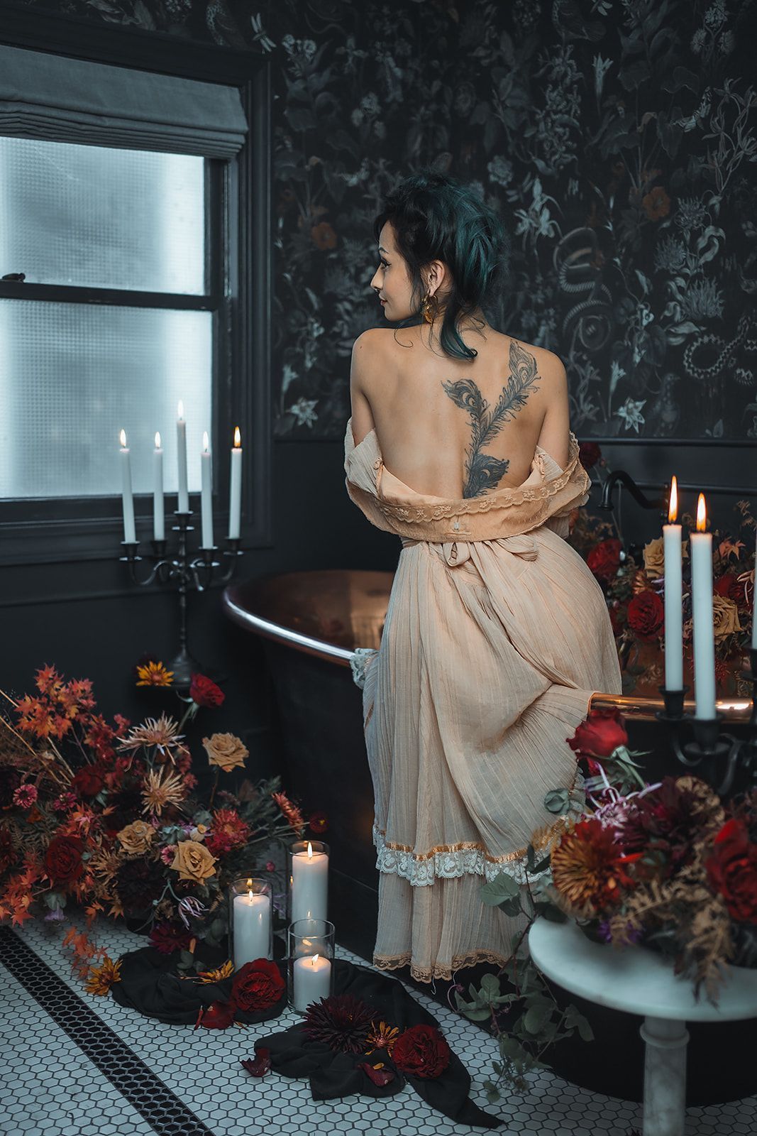 A woman in a dress is standing in a bathroom with candles and flowers.
