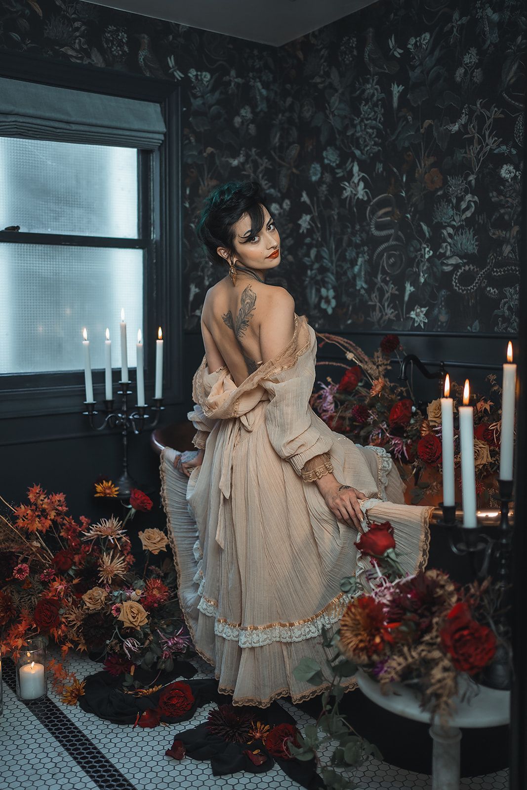 A woman in a dress is standing in a bathroom surrounded by candles and flowers.