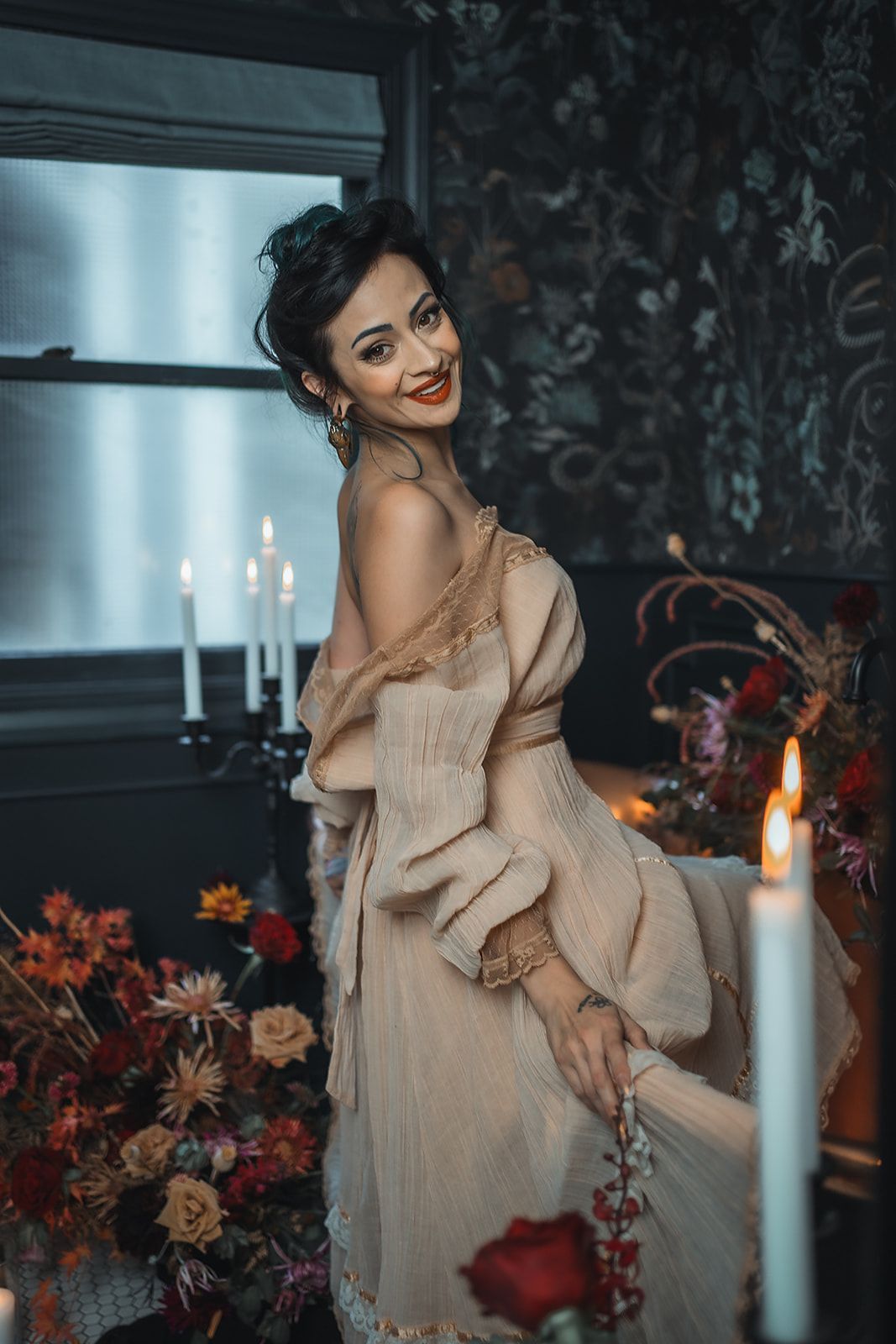 A woman in a dress is standing in a room with candles and flowers.