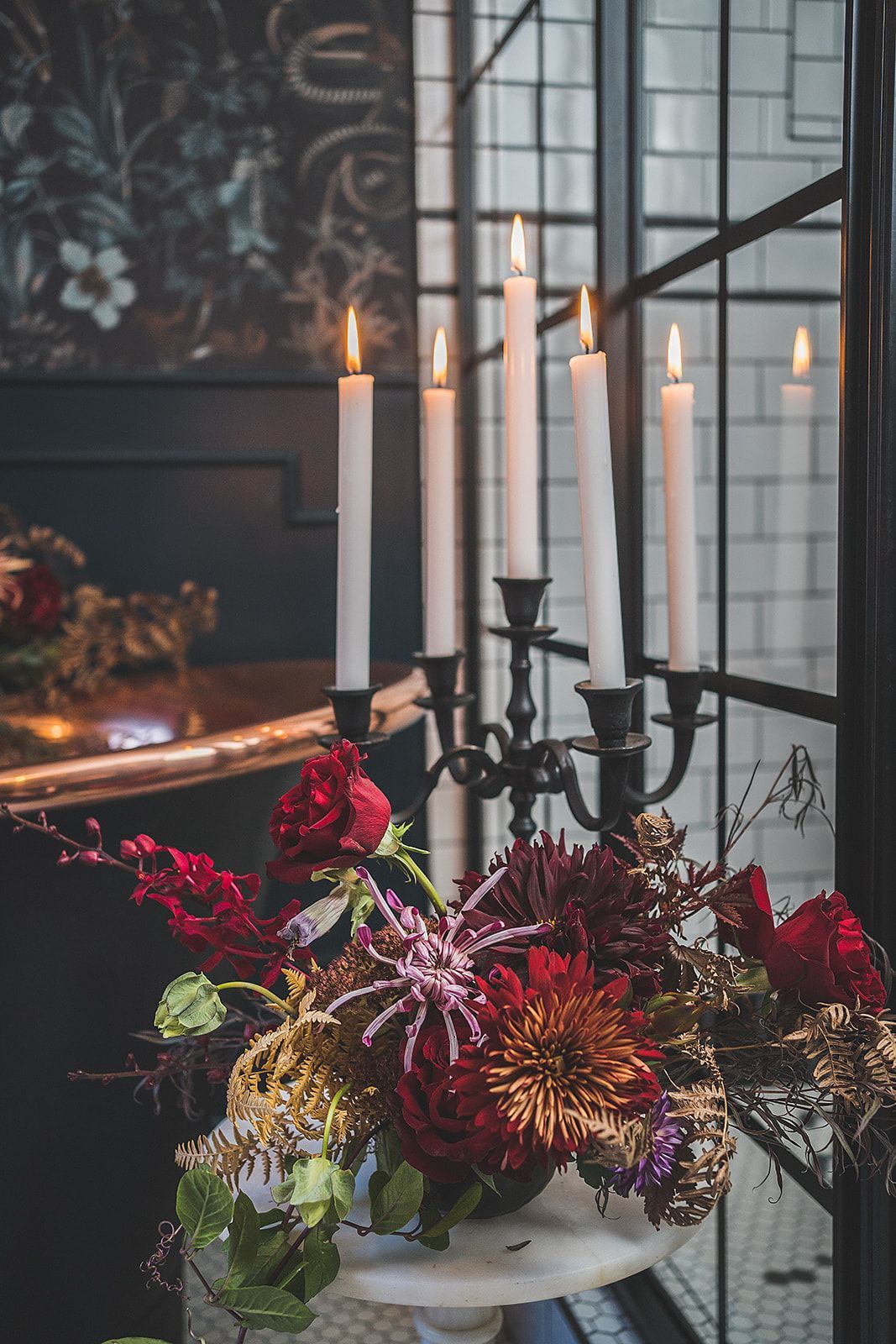 A vase of flowers and candles on a table in front of a window.