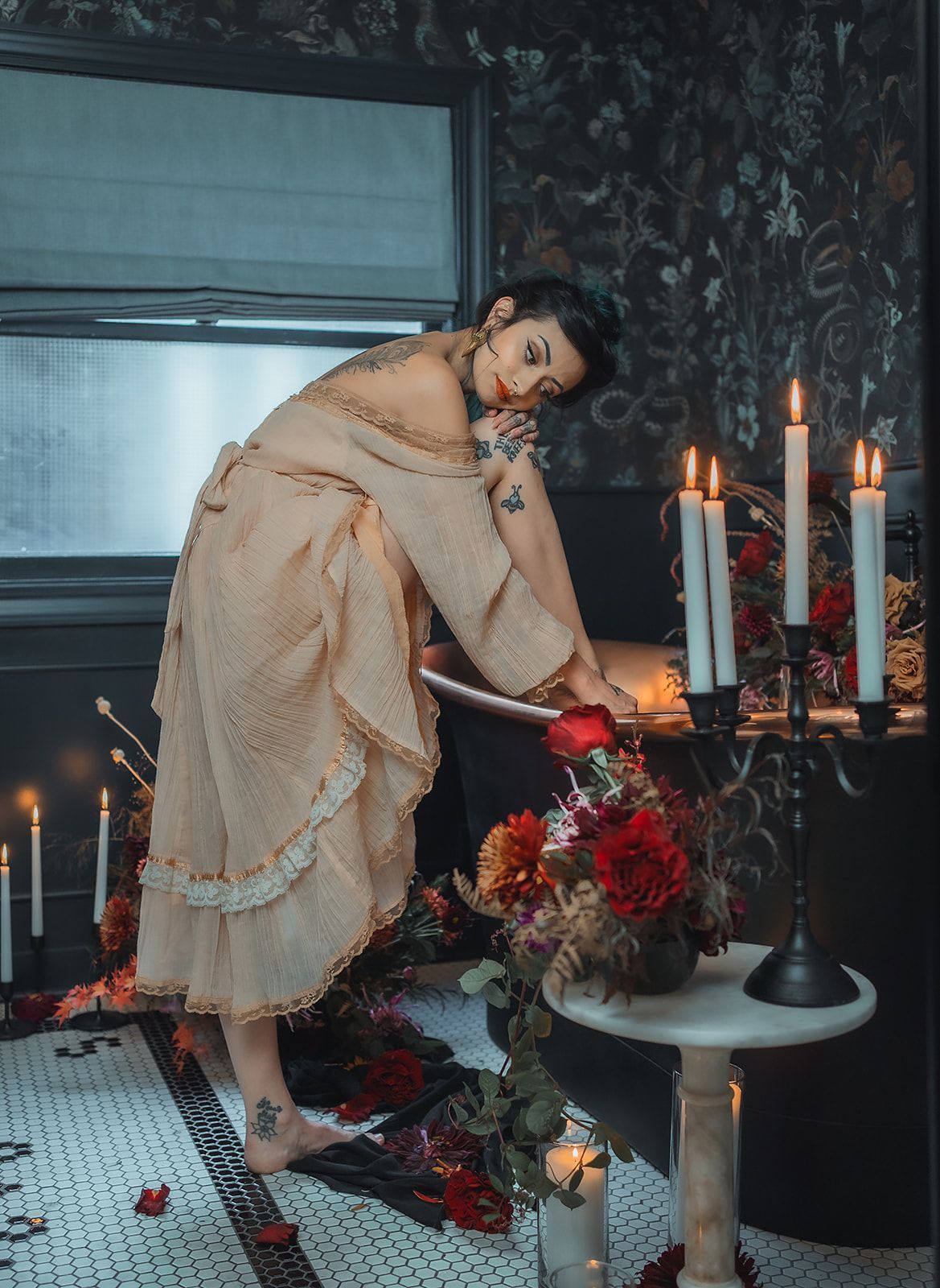 A woman is kneeling in a bathtub surrounded by candles and flowers.