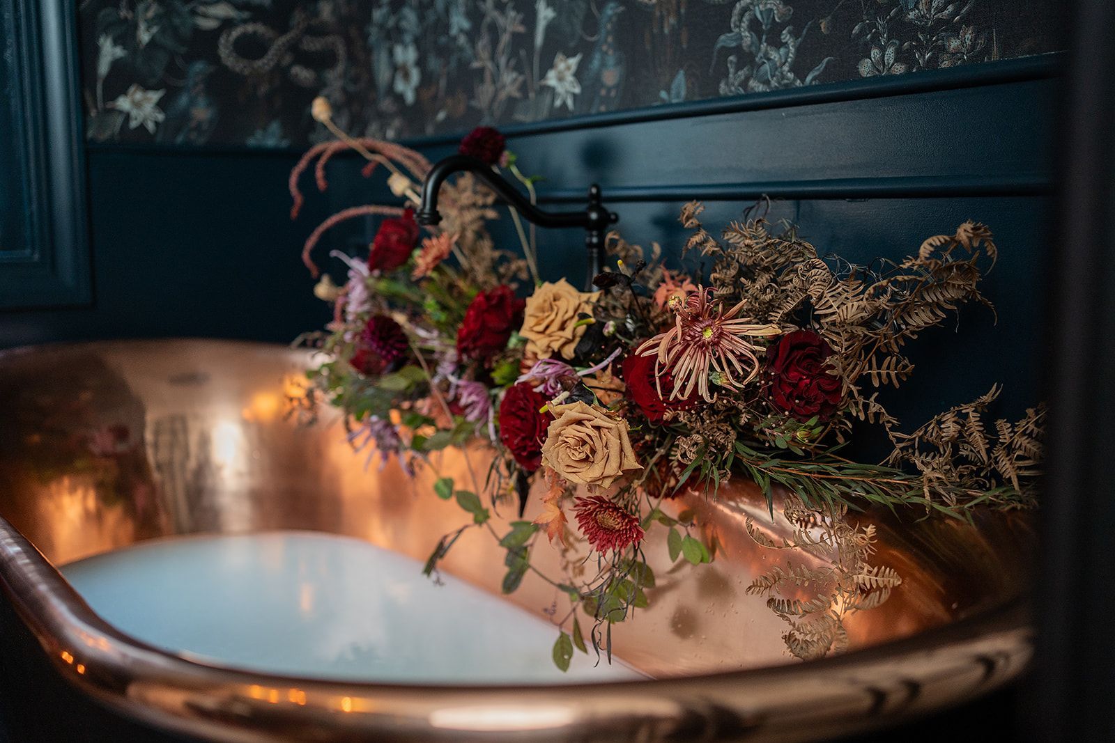 A copper sink with flowers in it in a bathroom.