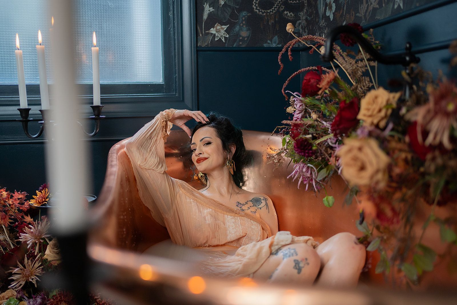 A woman is laying in a bathtub surrounded by flowers and candles.