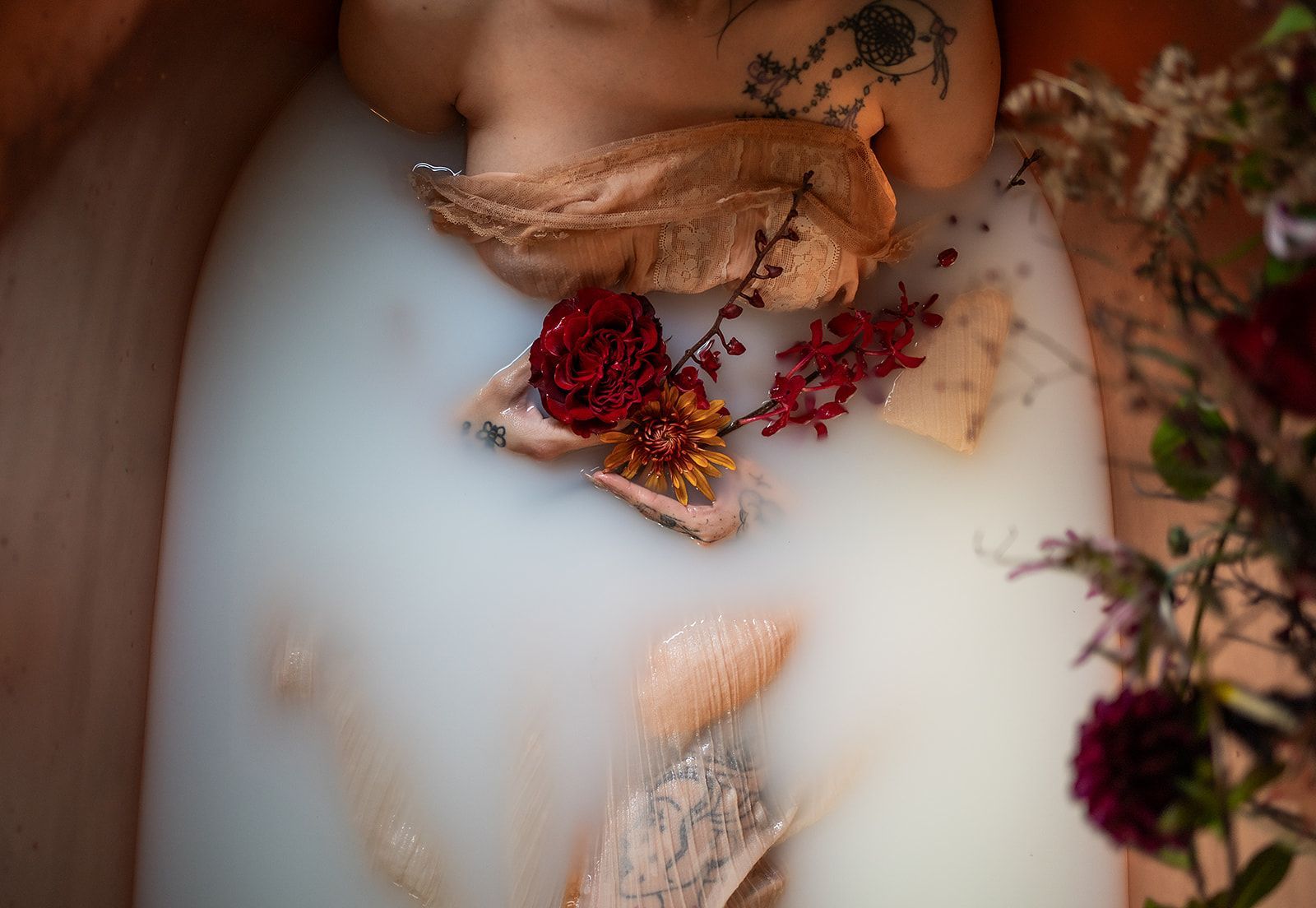 A woman is laying in a bathtub filled with milk and flowers.