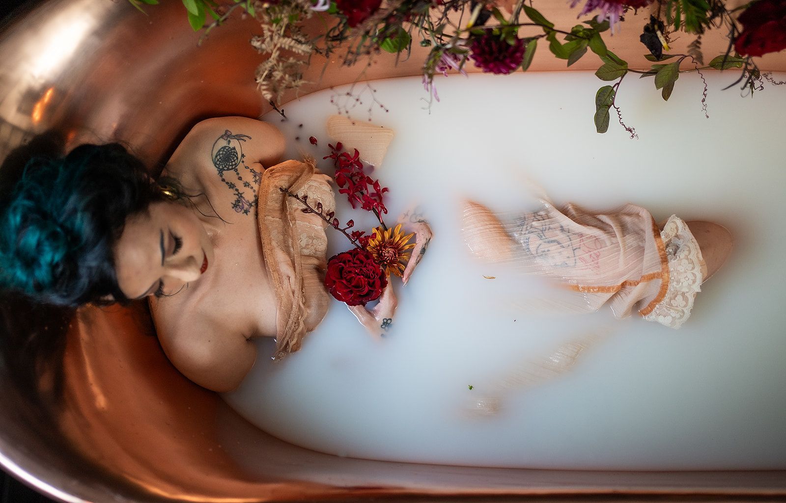 A woman is laying in a bathtub filled with milk and flowers.