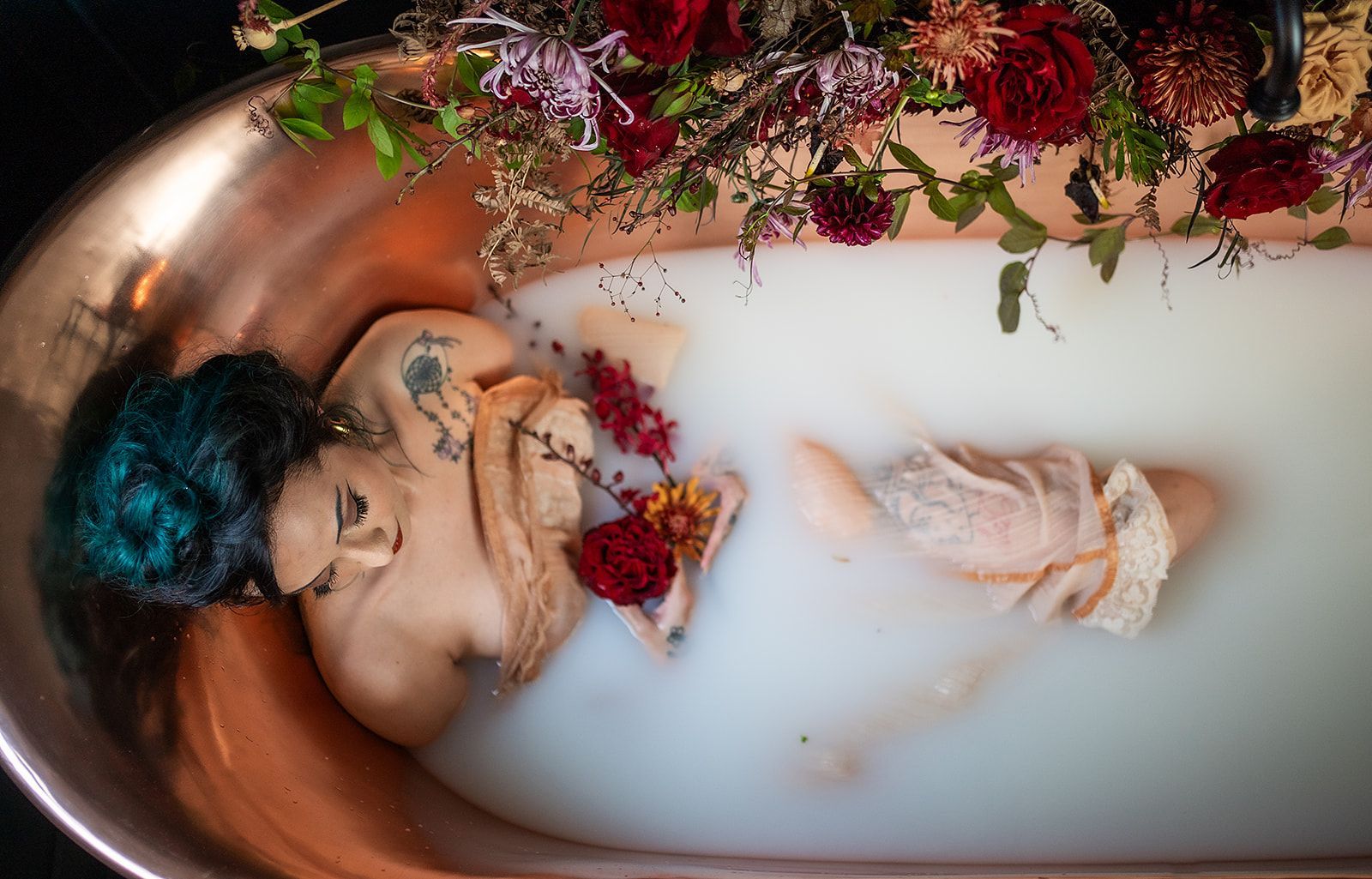 A woman is laying in a bathtub filled with milk and flowers.