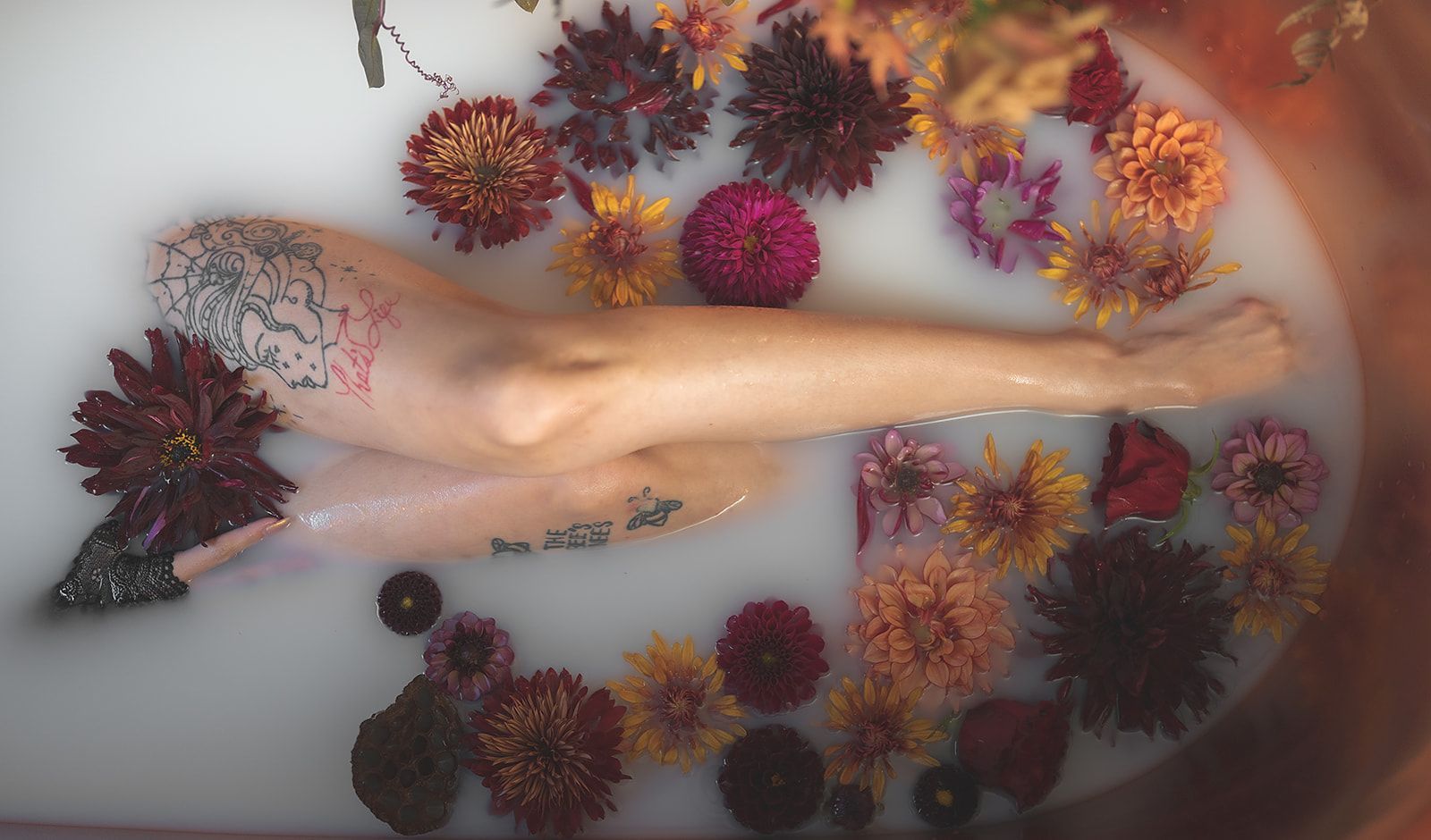 A womans legs in a milk bath with flowers around her.