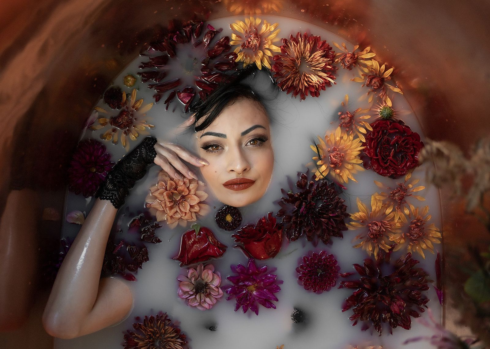 A woman is laying in a bathtub filled with milk and flowers.