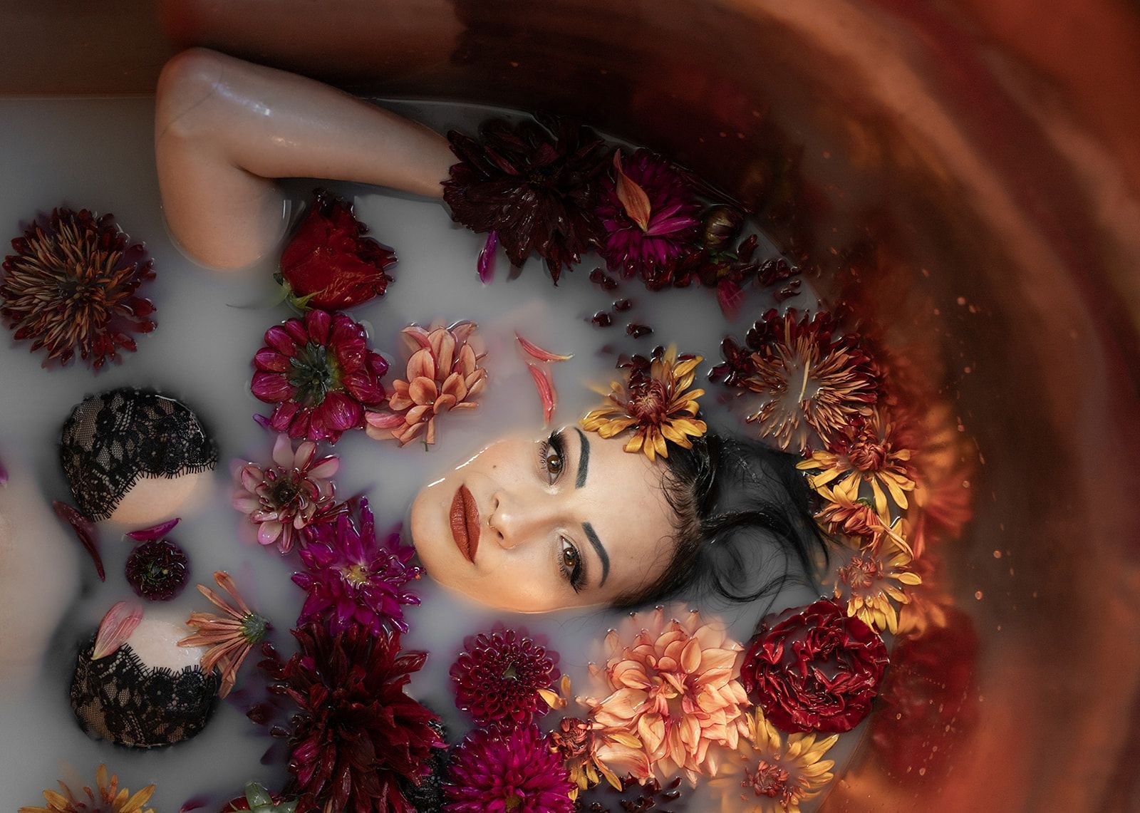 A woman is laying in a bathtub filled with milk and flowers.