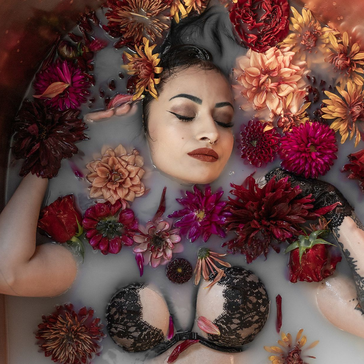 Woman with closed eyes, surrounded by colorful flowers, in a milk bath, wearing a lace bra.