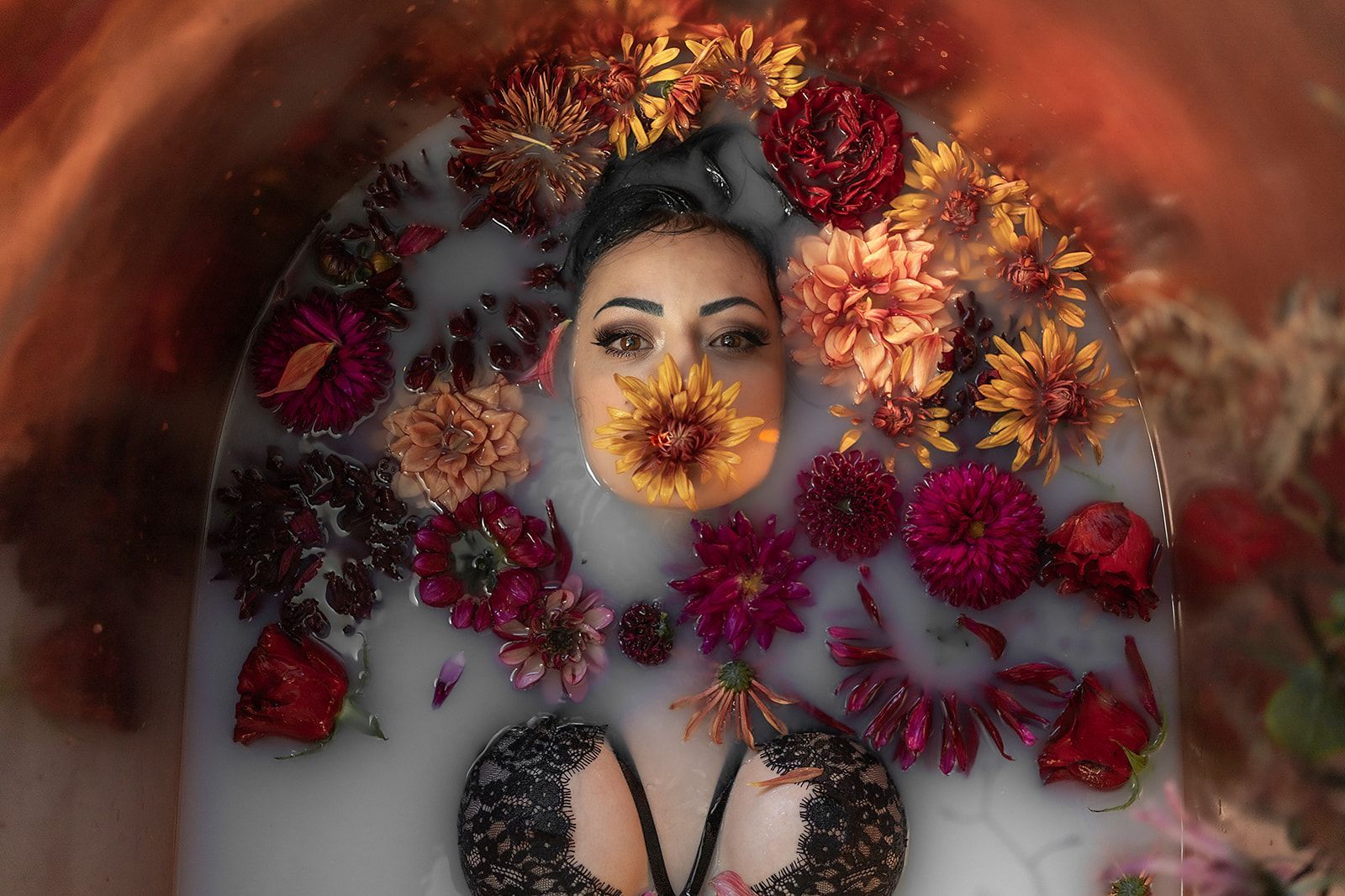 A woman is laying in a bathtub filled with milk and flowers.