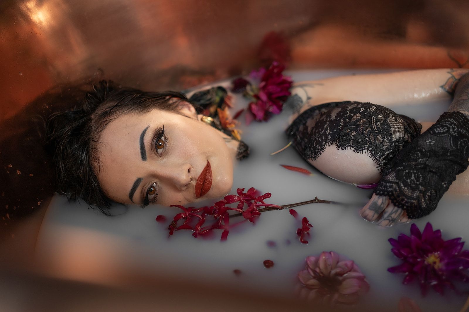 A woman is lying in a bathtub filled with milk and flowers.