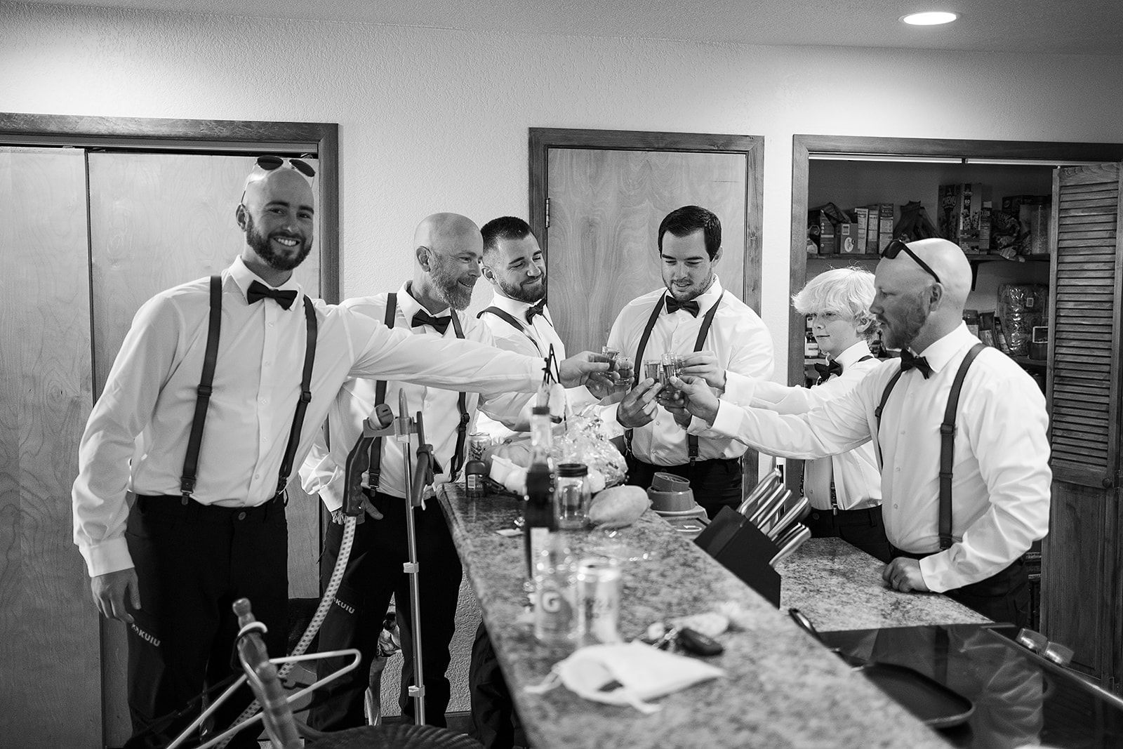 A group of men in tuxedos and suspenders are toasting each other in a black and white photo.