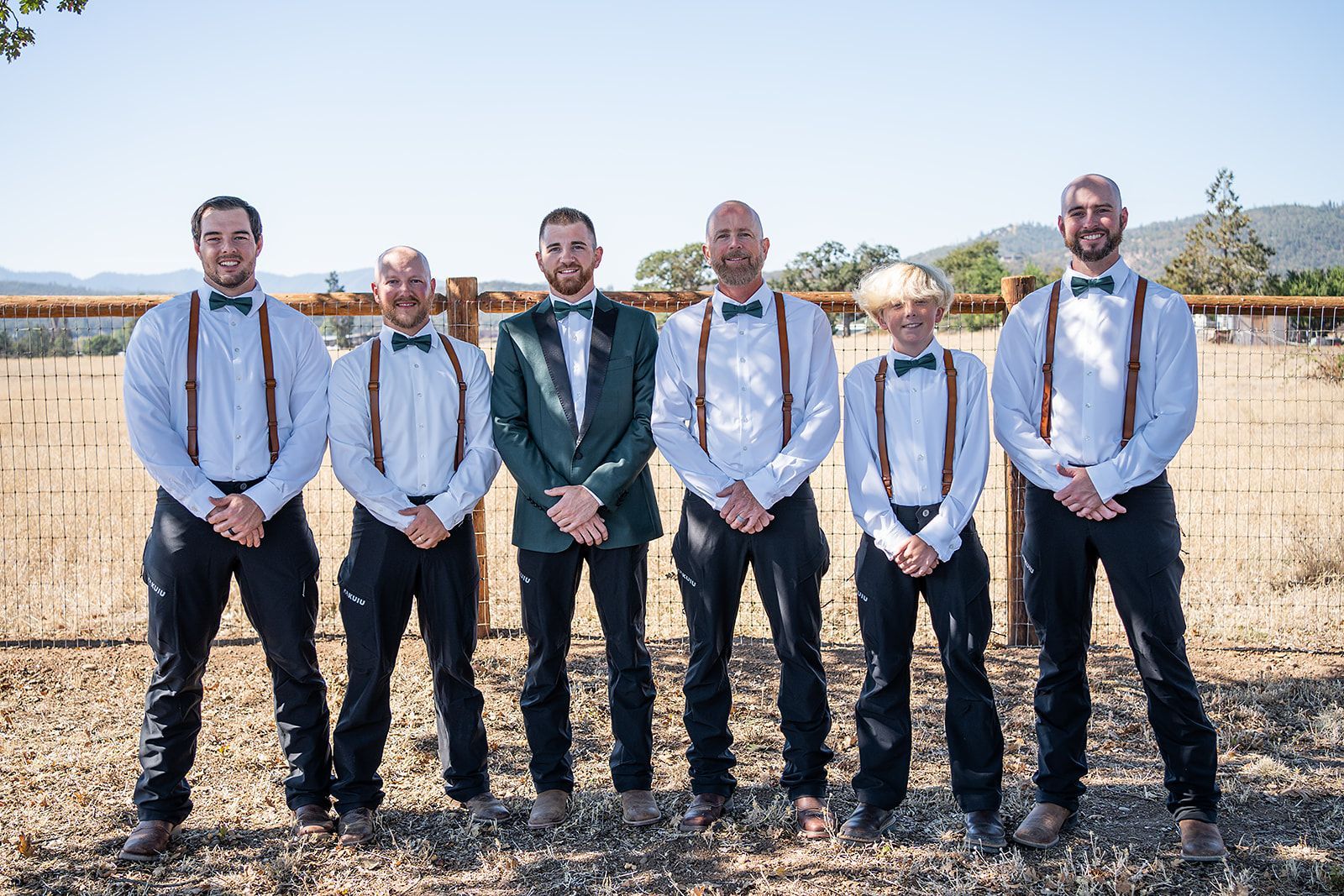 The groom and his groomsmen are posing for a picture in front of a fence.