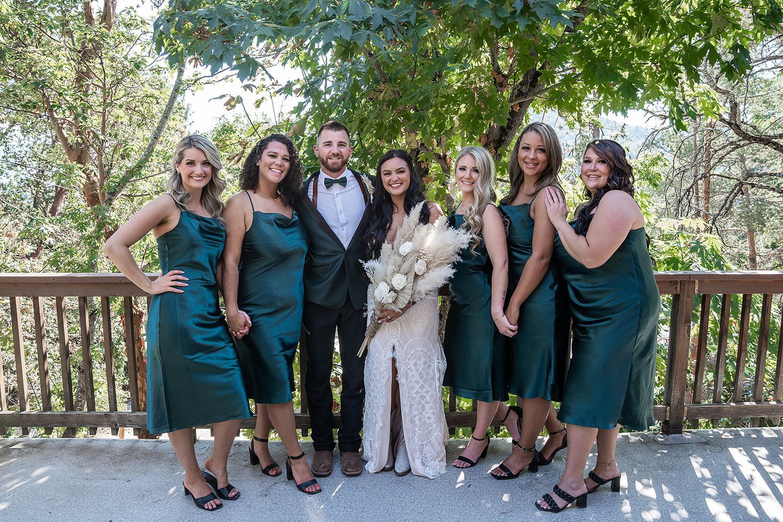The bride and groom are posing for a picture with their bridesmaids in green dresses.