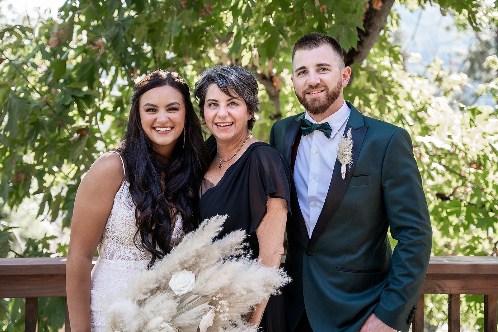 A bride and groom are posing for a picture with their mother.