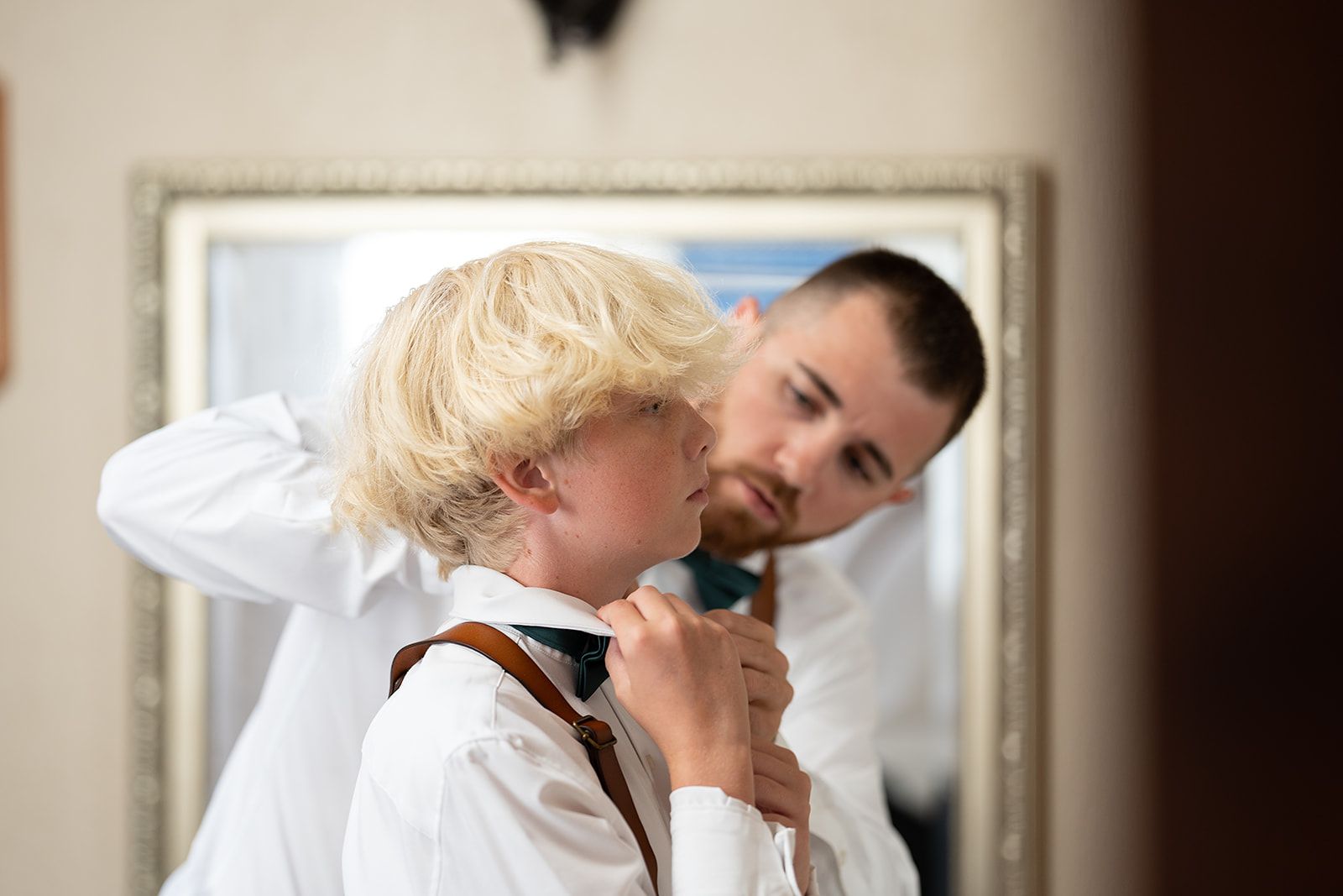 A man is helping a boy with his bow tie in front of a mirror.
