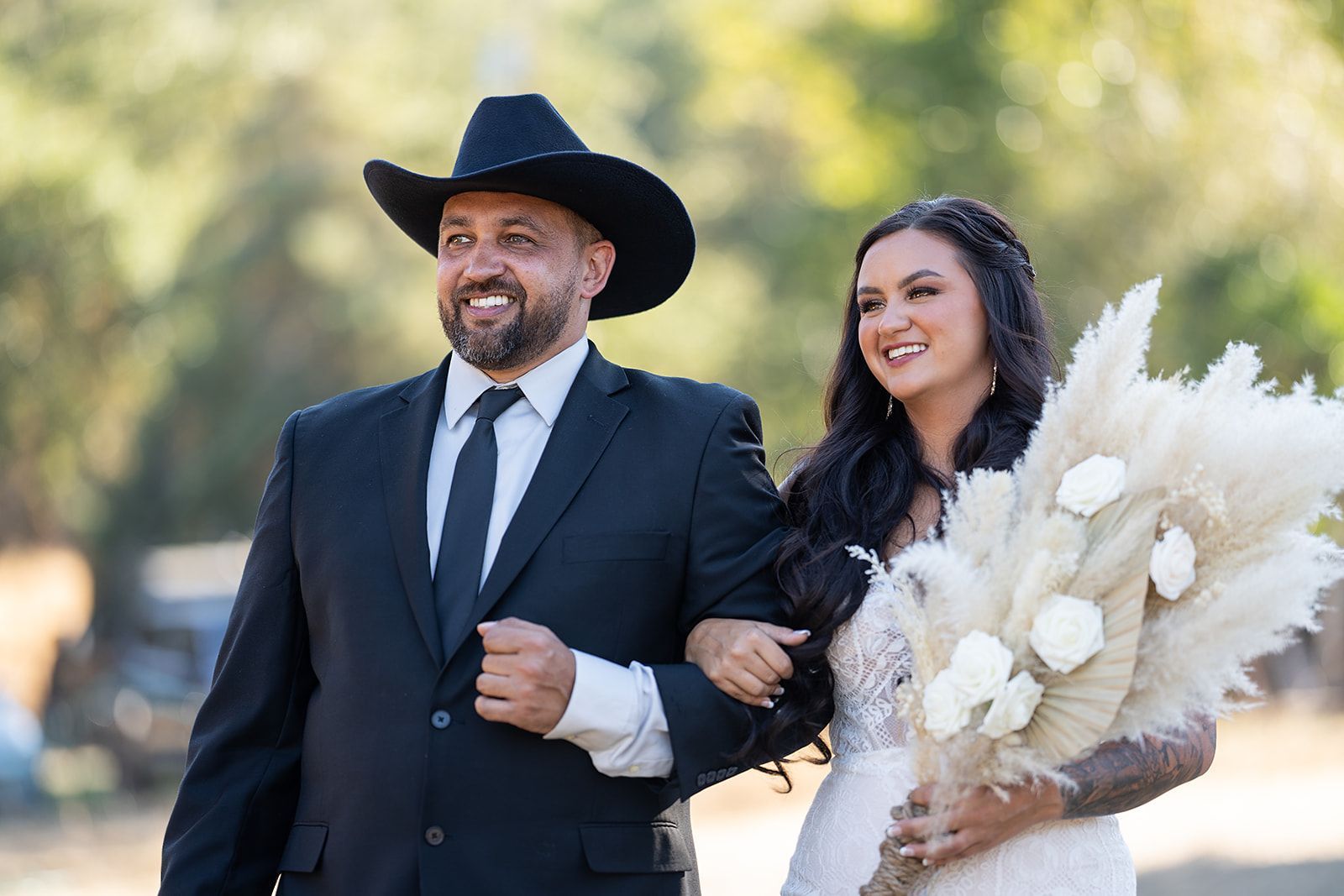 A bride and groom are walking down the aisle at their wedding . the bride is wearing a cowboy hat.