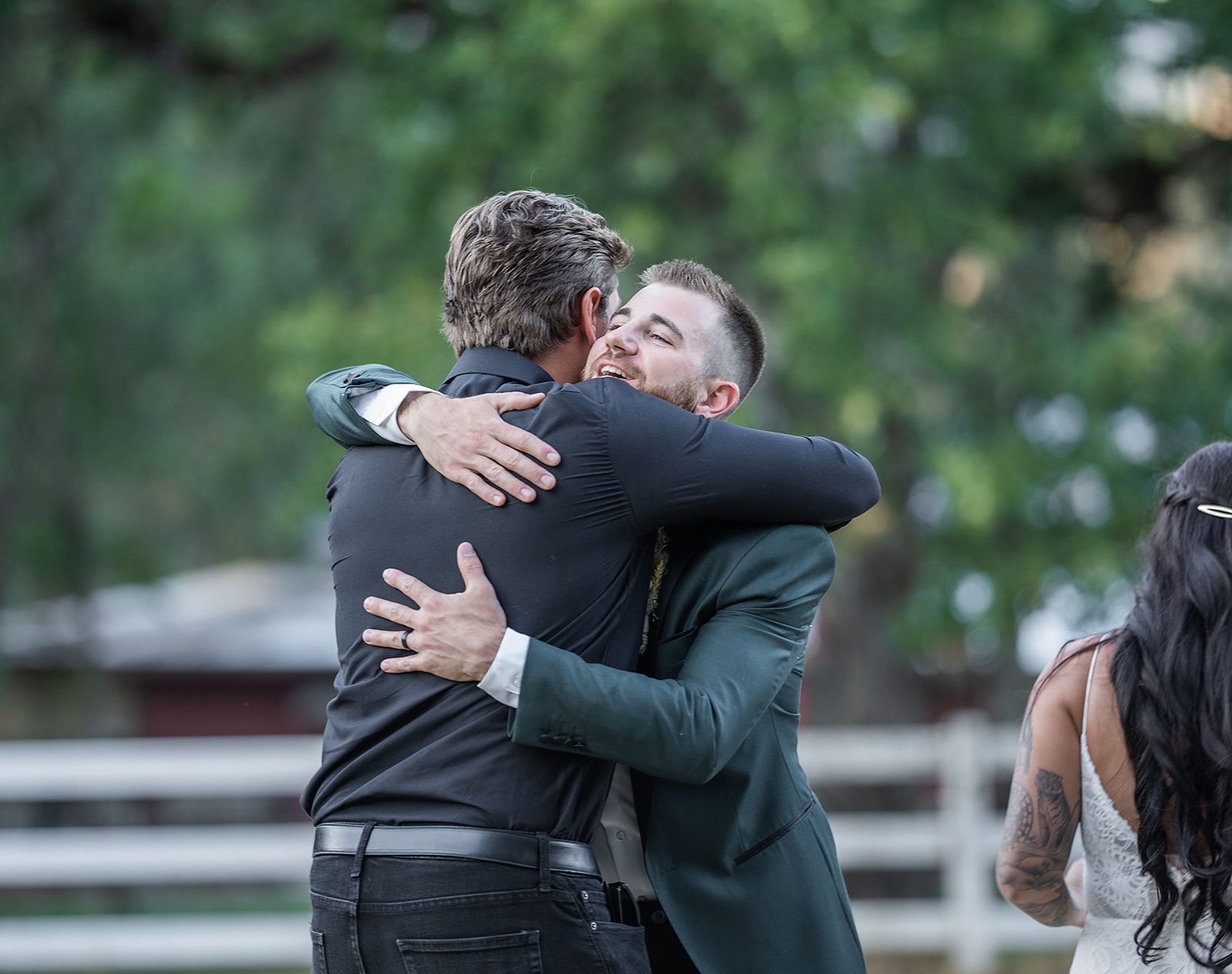 A man in a suit is hugging another man in a black shirt.