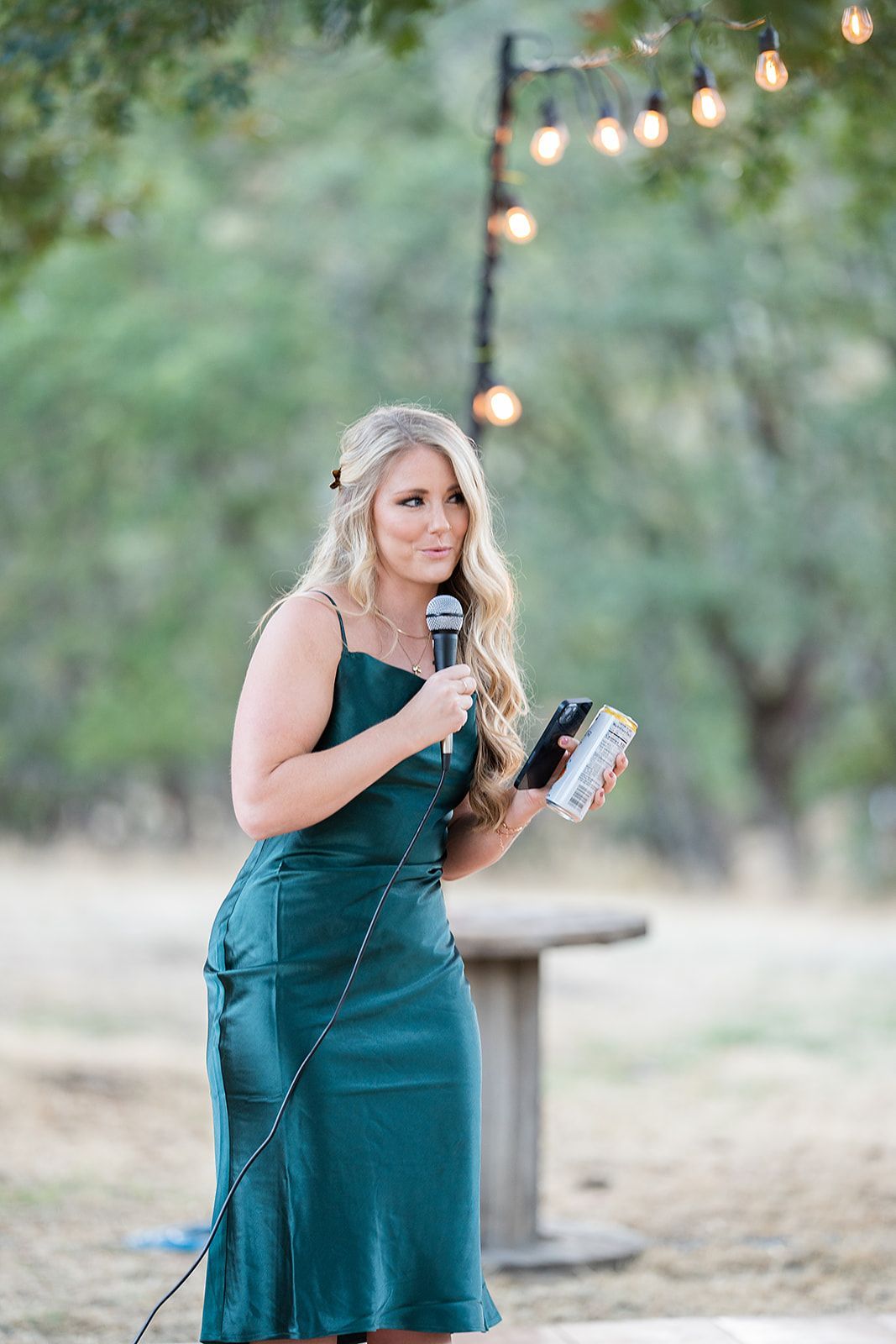 A woman in a green dress is holding a microphone and a cell phone.