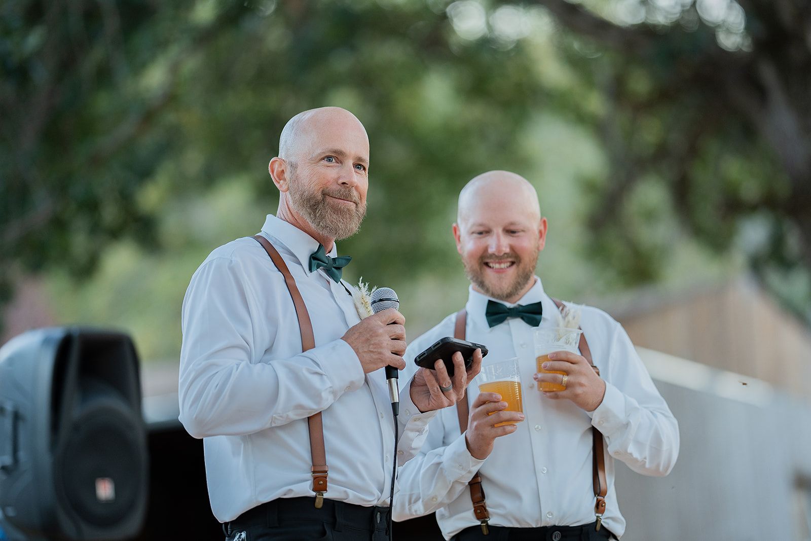Two men are standing next to each other holding drinks and a microphone.