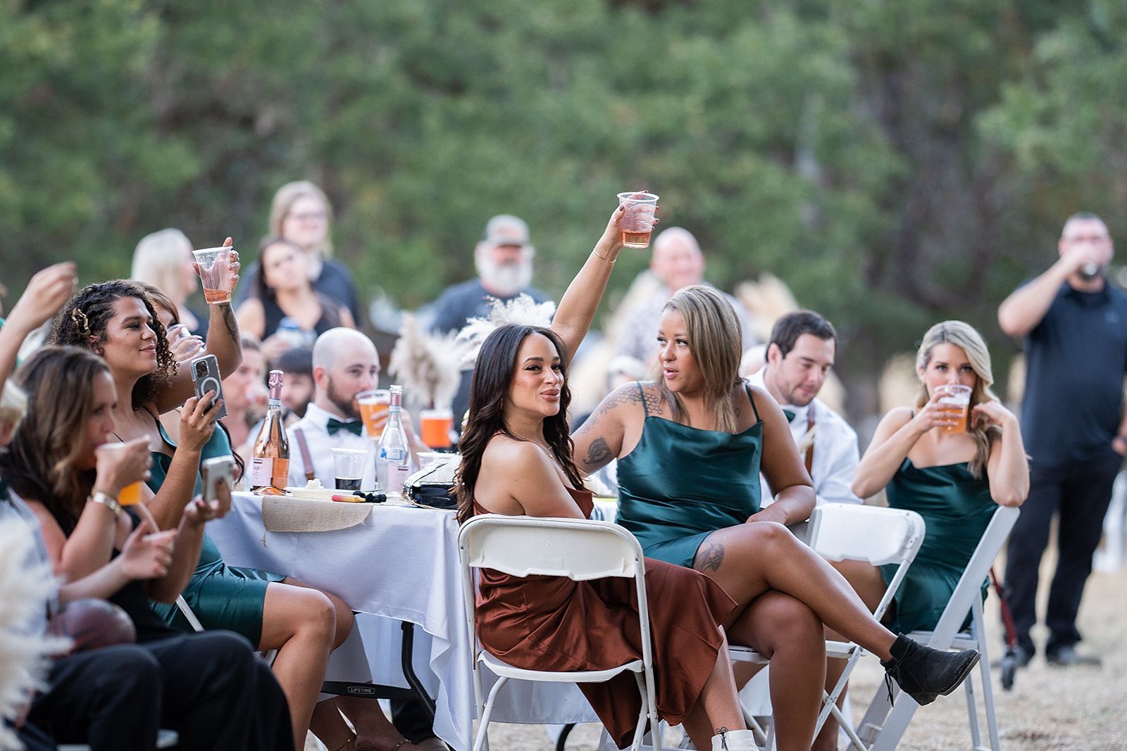 A group of people are sitting at tables and chairs raising their glasses in the air.