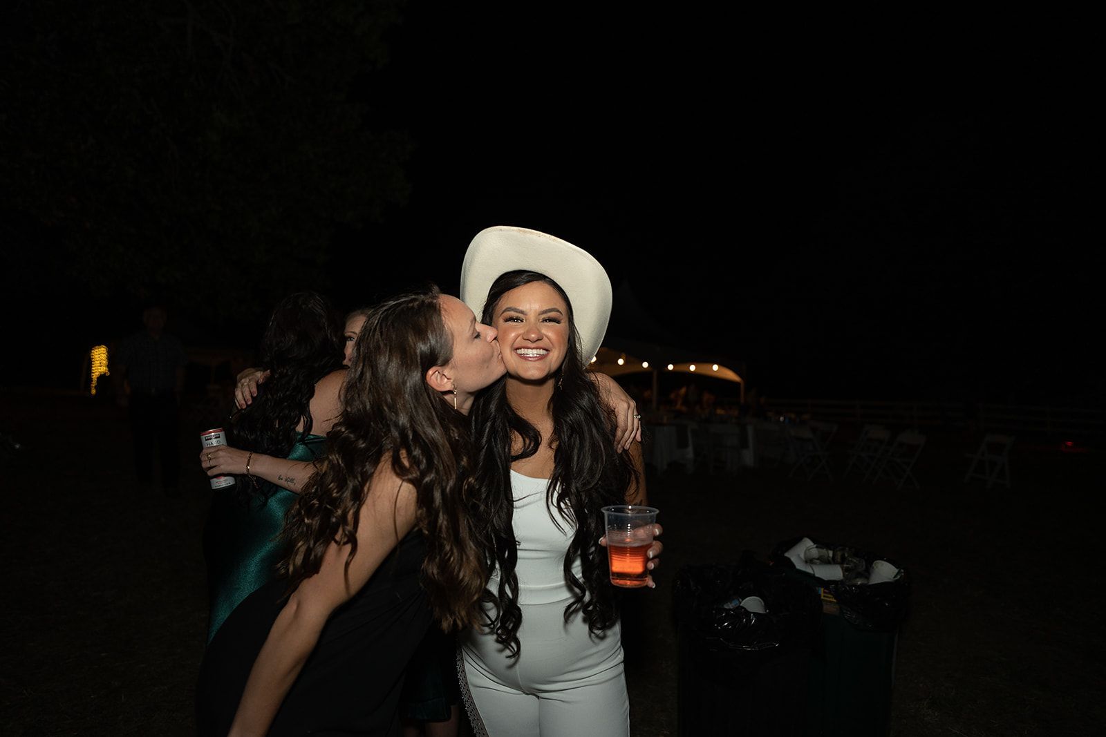A woman in a cowboy hat is kissing another woman on the cheek.