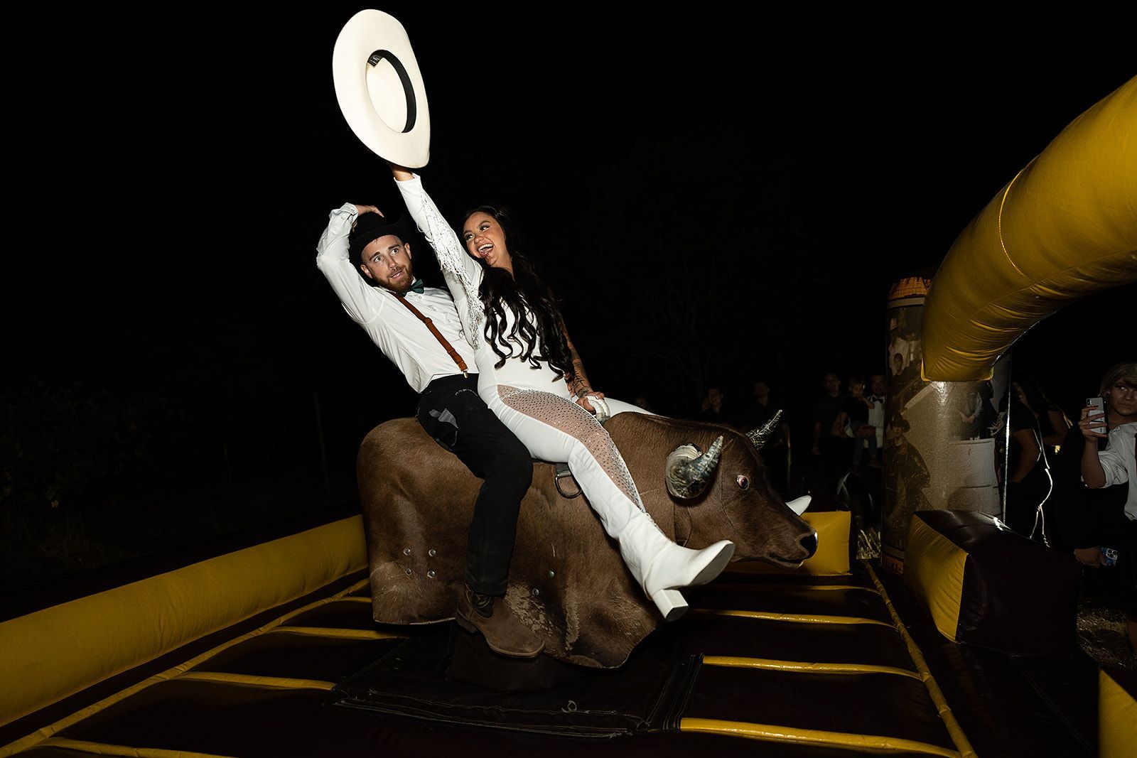 A man and a woman are riding a bull at night.