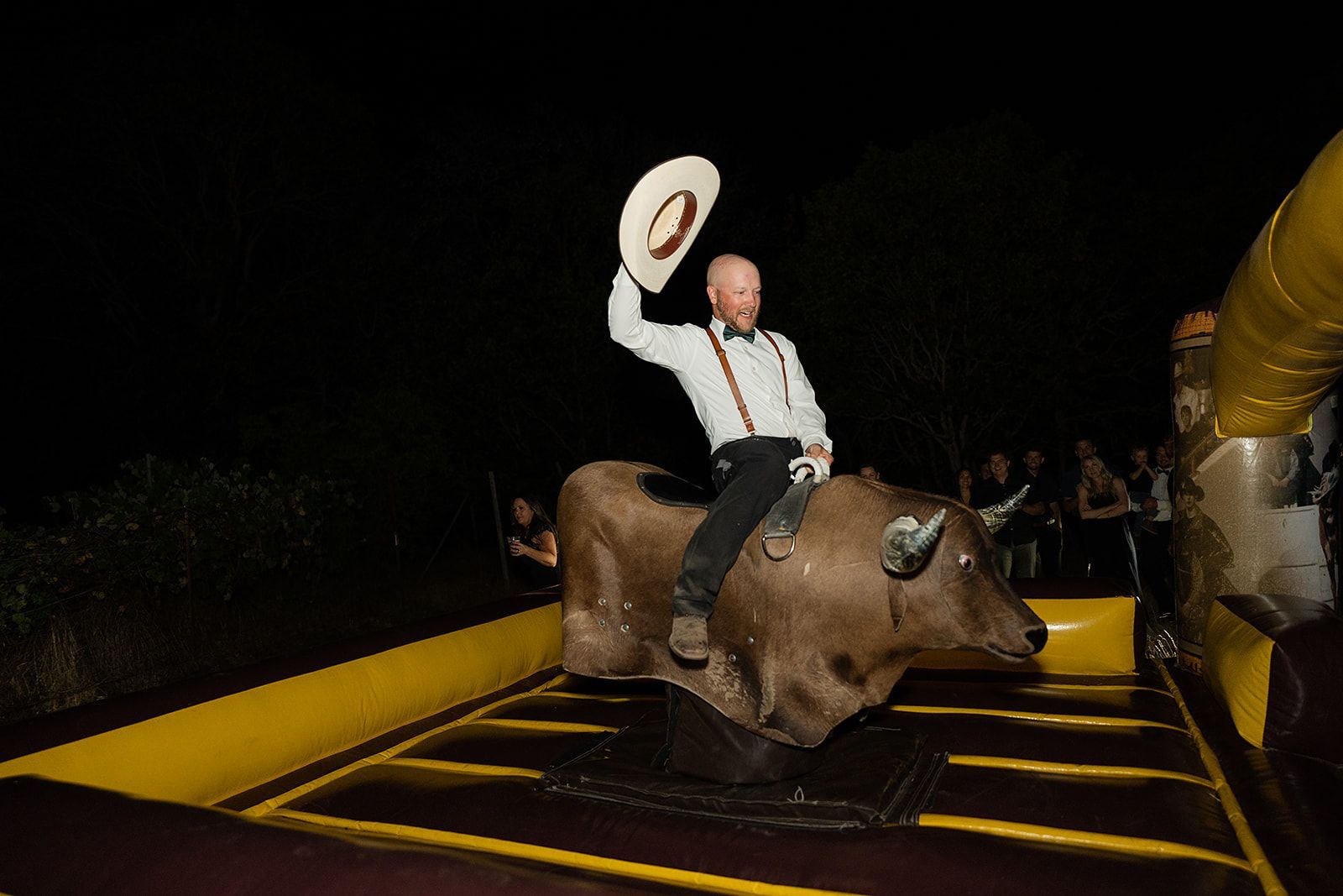 A man is riding a bull on a bouncy castle at night.