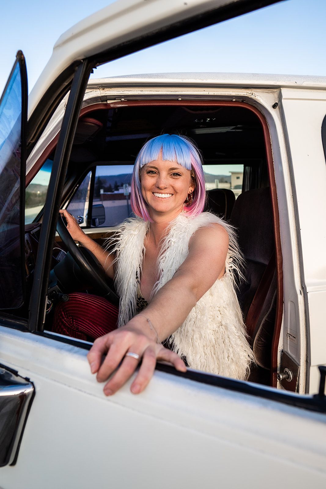 A woman in a pink wig is sitting in the driver 's seat of a white truck.