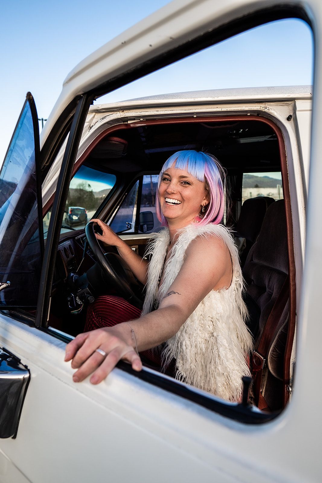 A woman with pink hair is sitting in the driver 's seat of a white truck.