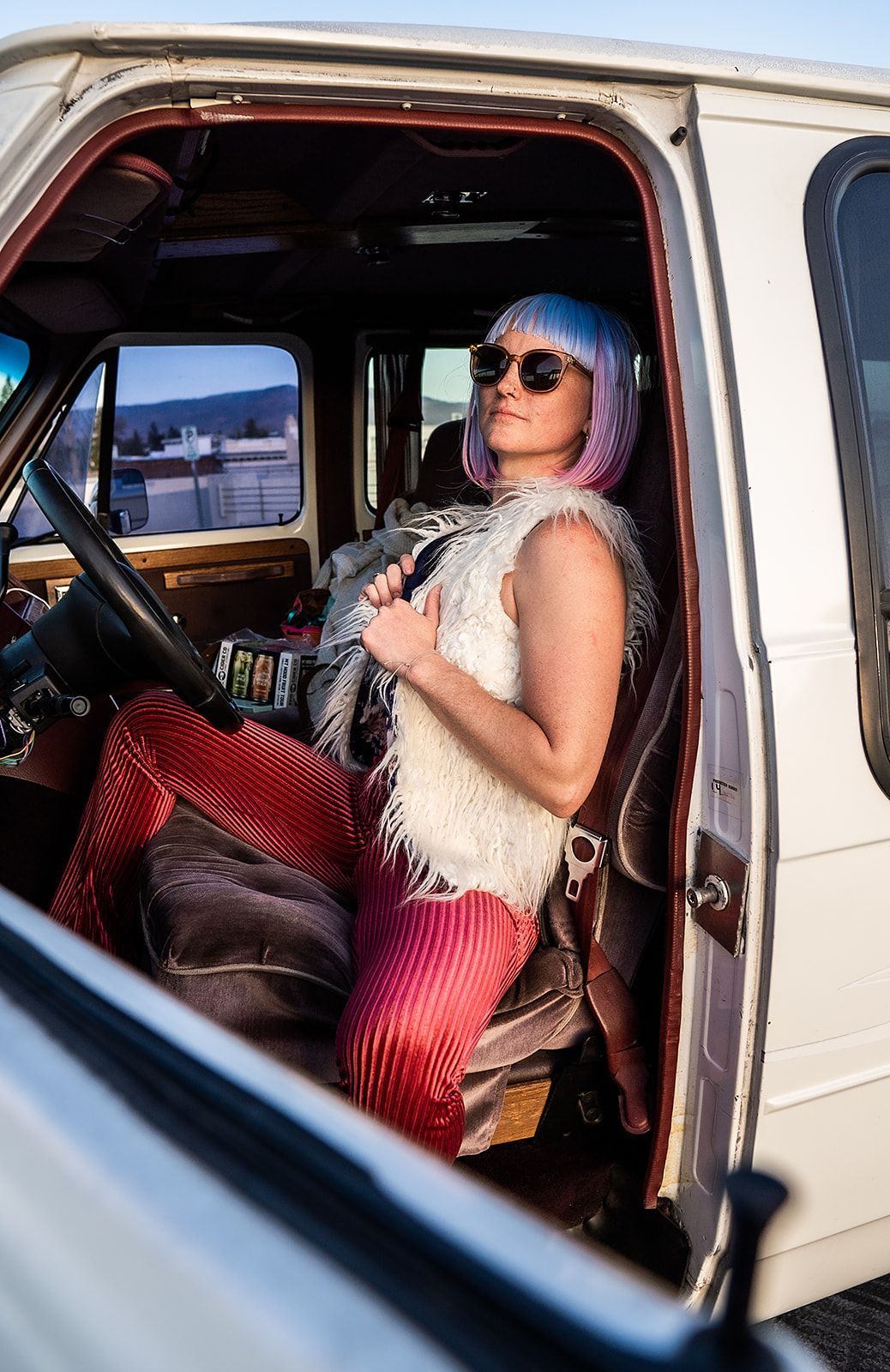 A woman with pink hair is sitting in the driver 's seat of a white van.