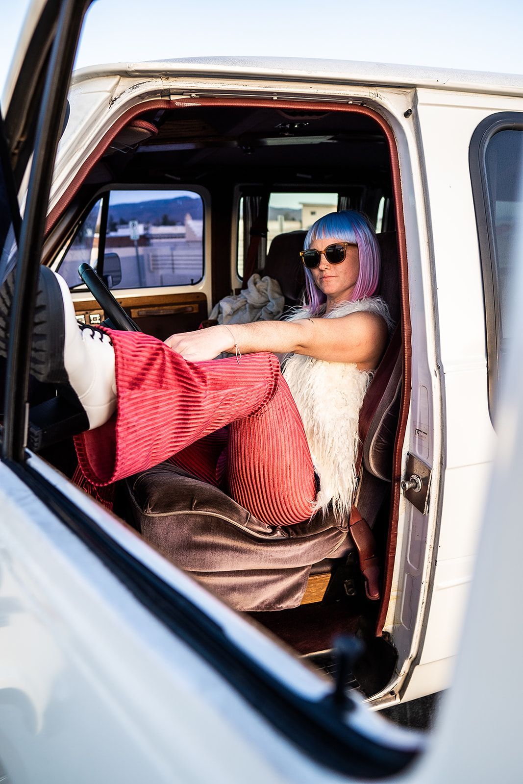 A woman with pink hair is sitting in the back seat of a white van.