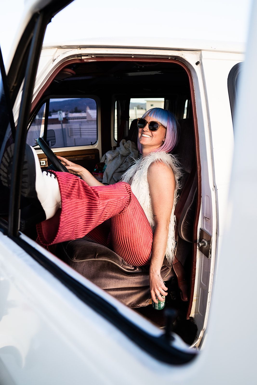 A woman with pink hair is sitting in the back seat of a white van.