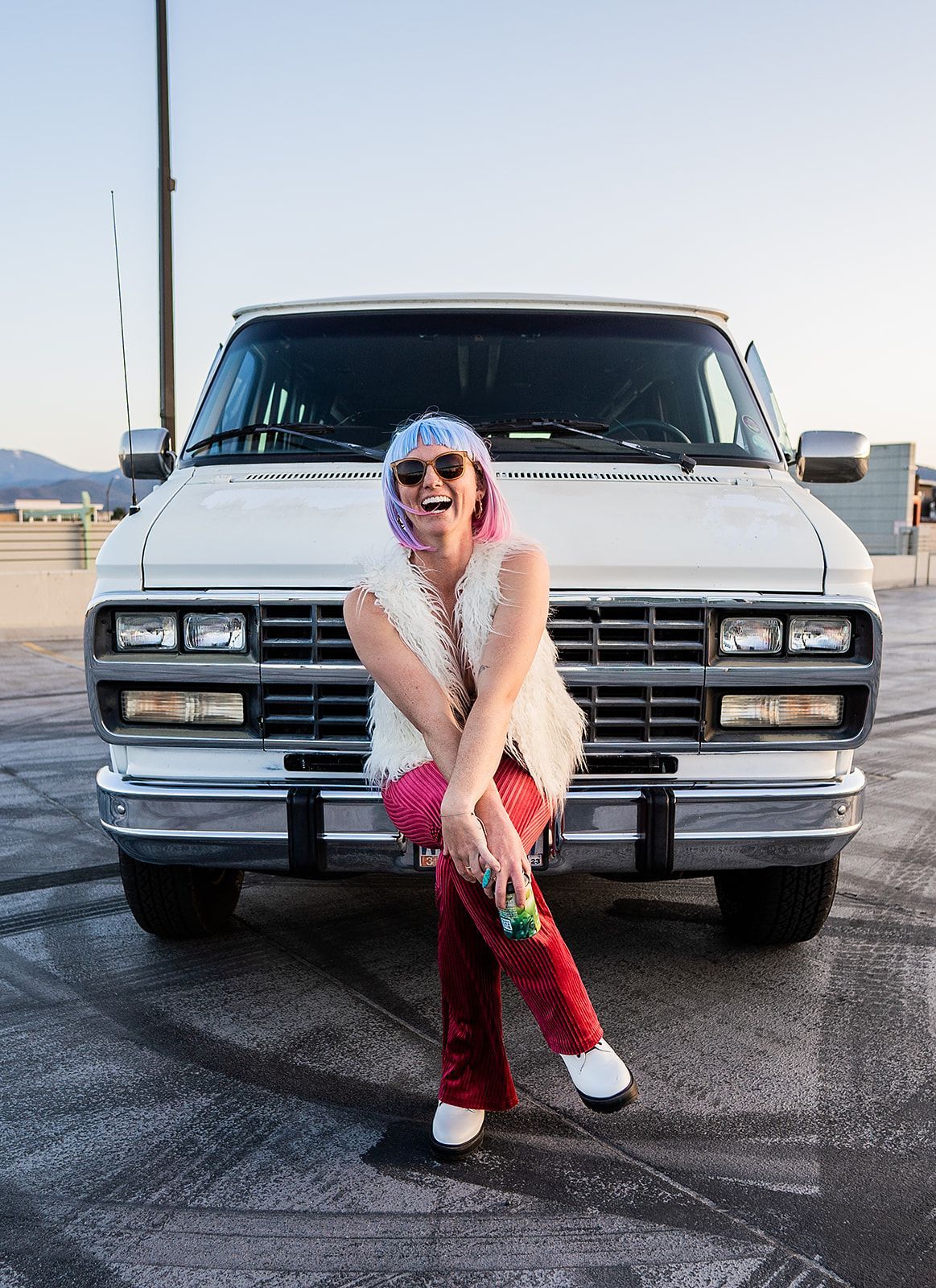 A woman is sitting on the front of a white van.