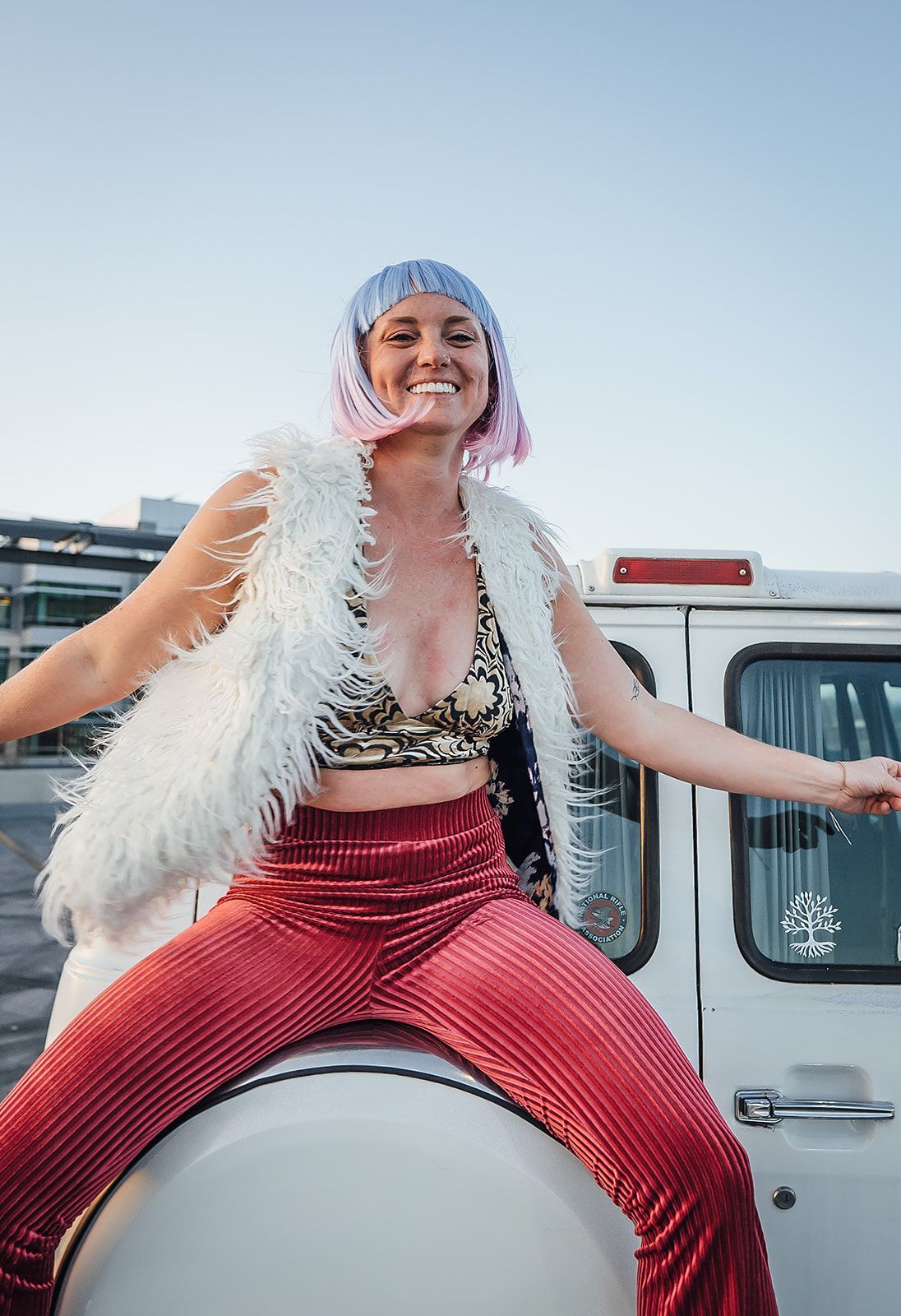A woman with pink hair is sitting on the back of a white van.