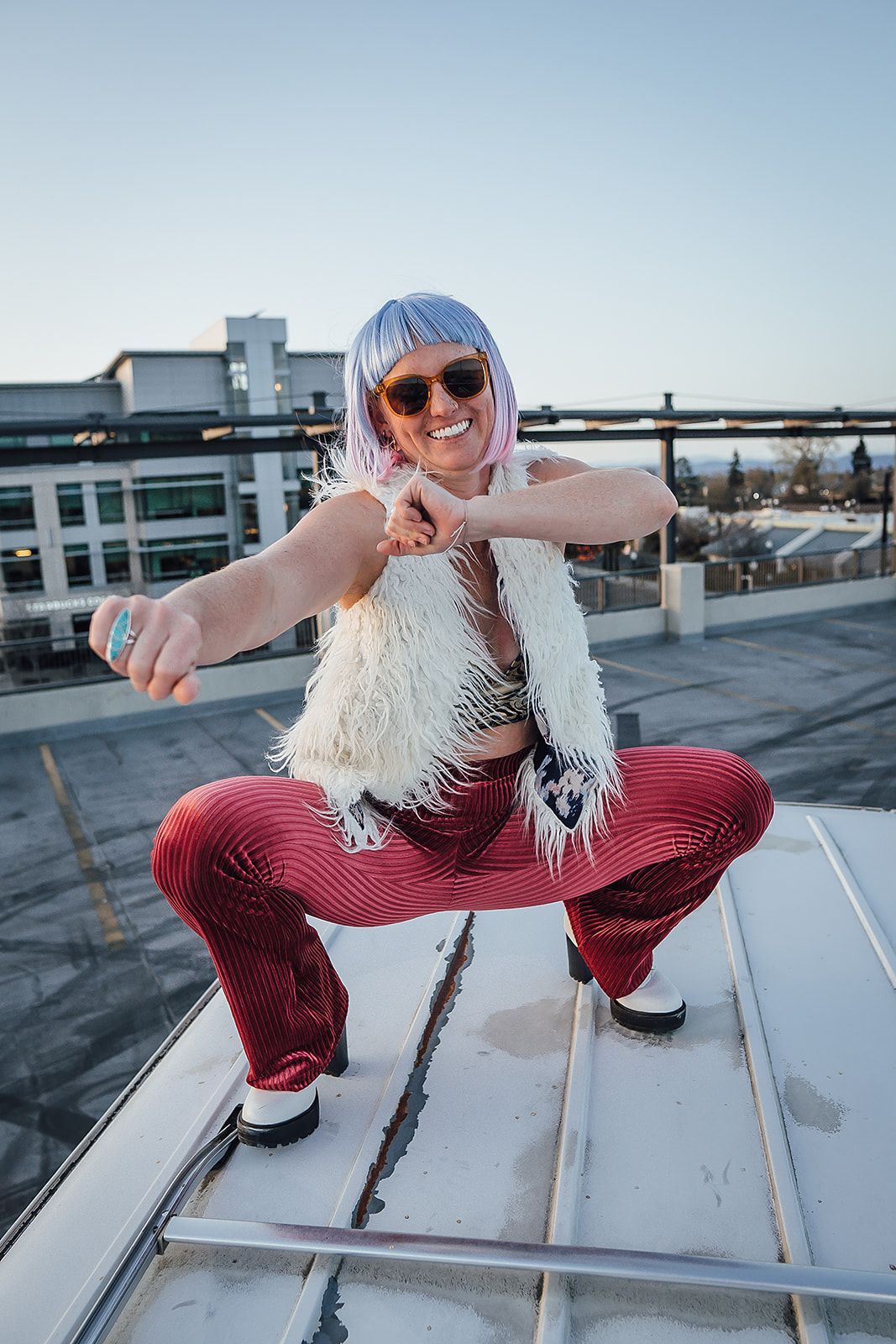 A man is squatting on a roof wearing a white vest and red pants.