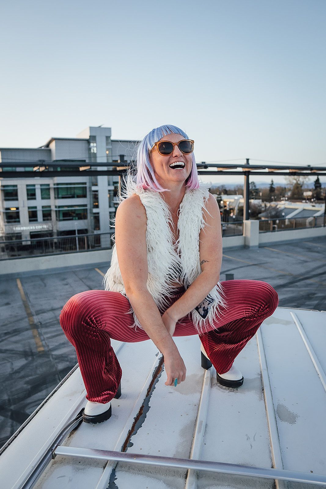 A woman is squatting on a roof wearing red sequined pants and a white vest.