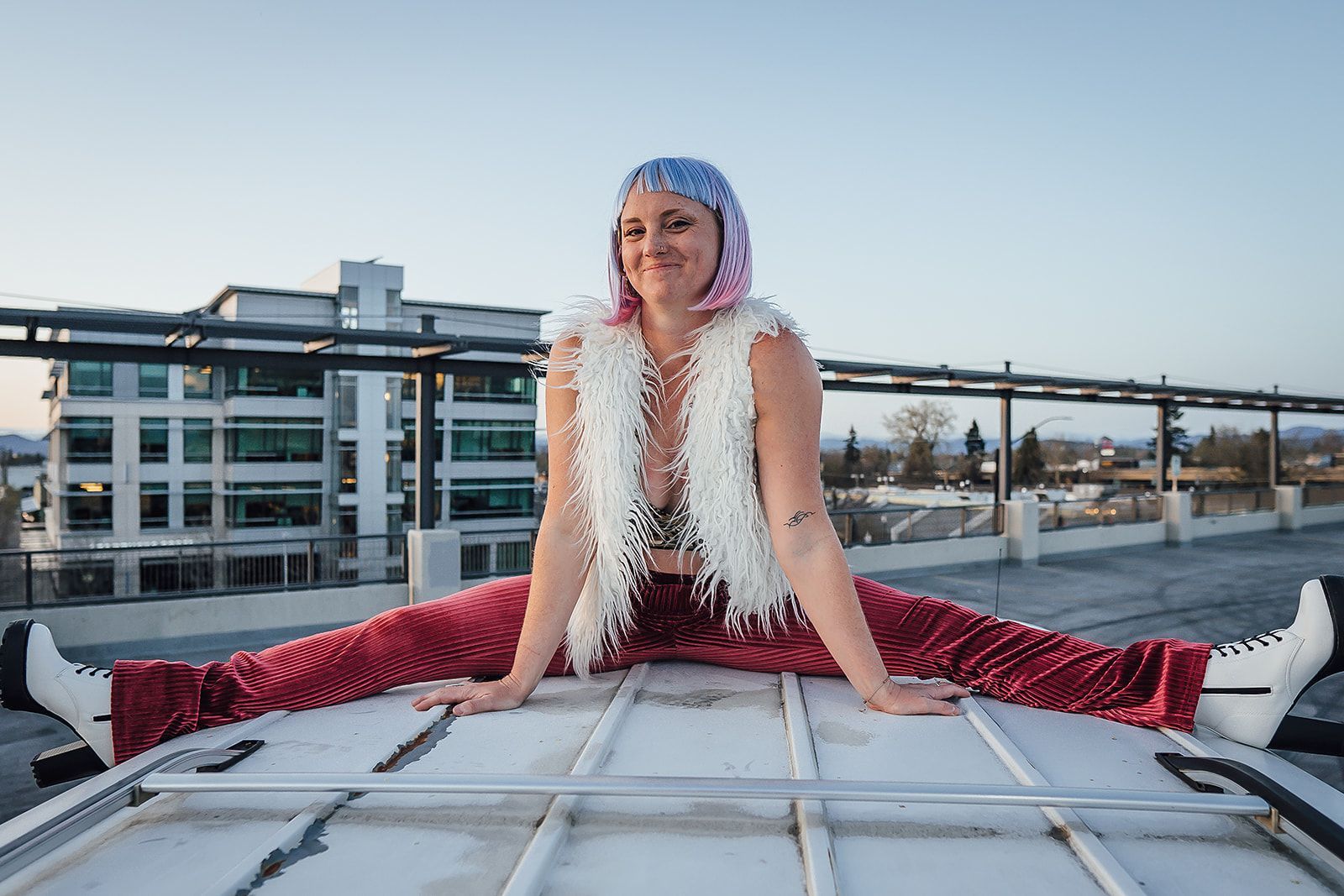 A woman is doing a split on the roof of a van.