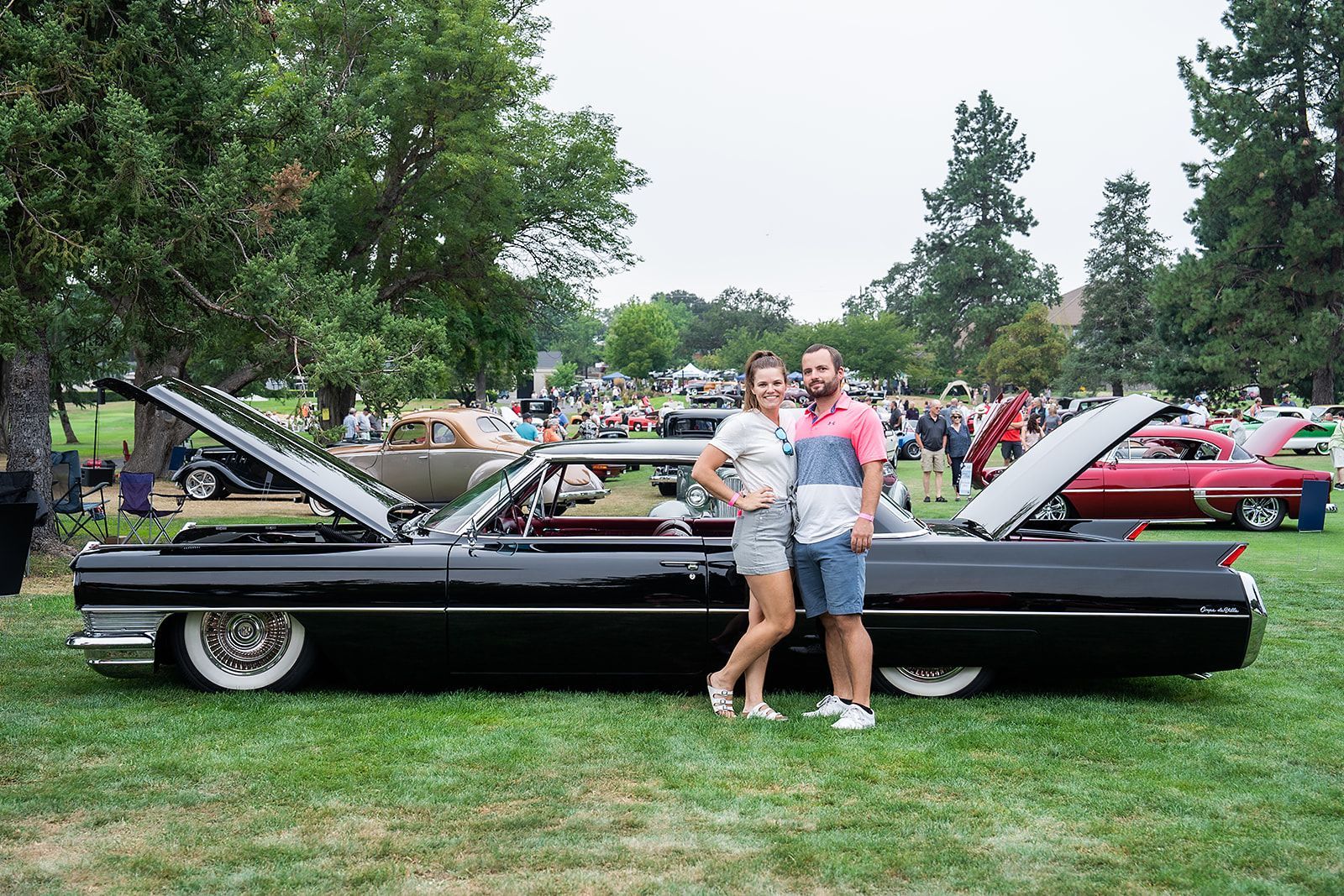 A man and a woman are standing next to a car at a car show.