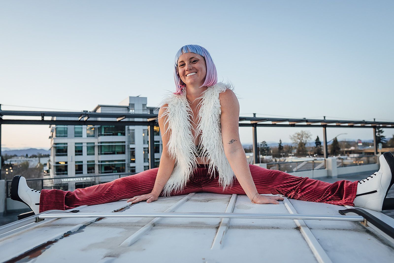 A woman is sitting on the roof of a building doing a split.