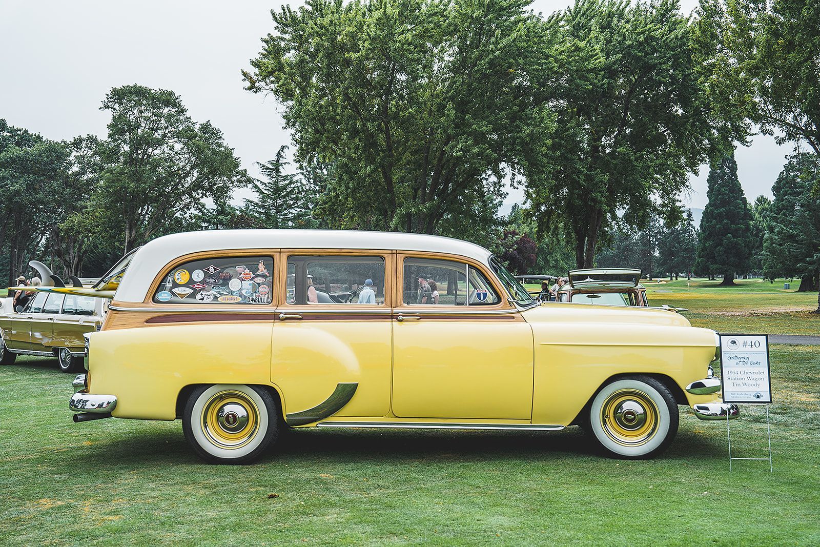 A yellow and white vintage car is parked in a grassy field.