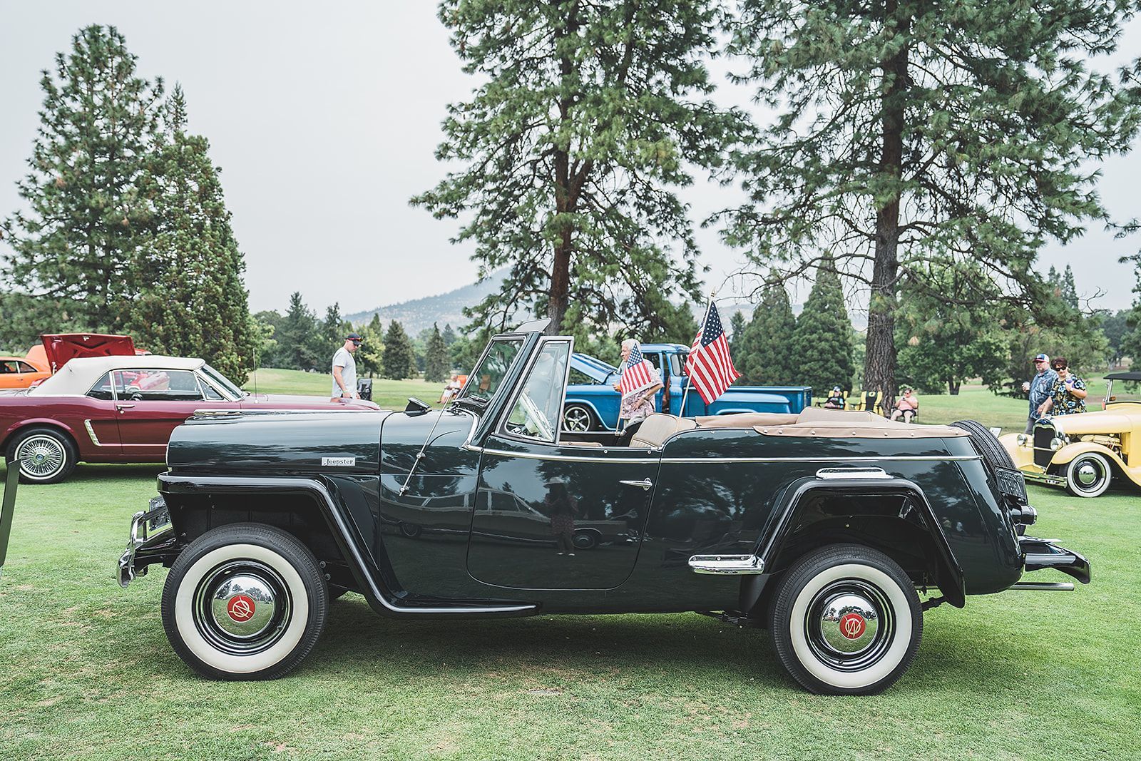 A black convertible jeep is parked in the grass at a car show.