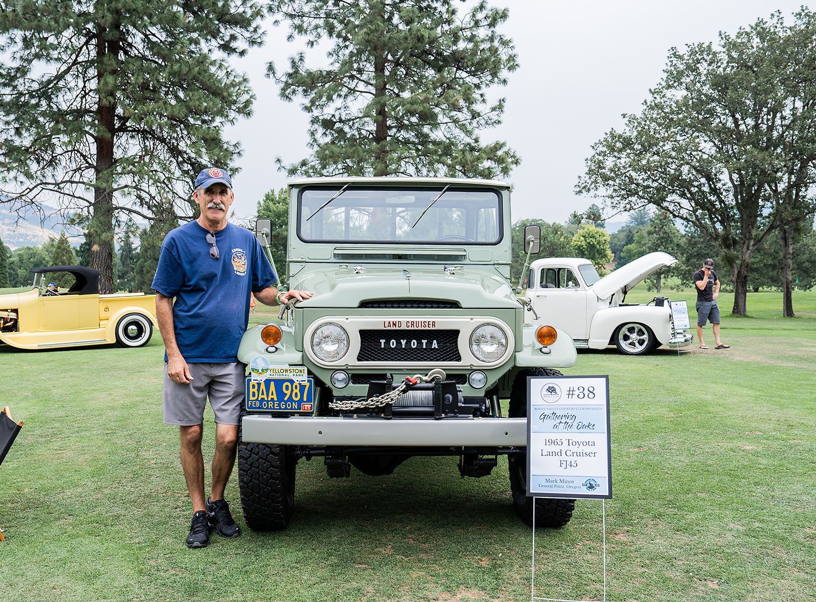 A man is standing in front of a green jeep at a car show.