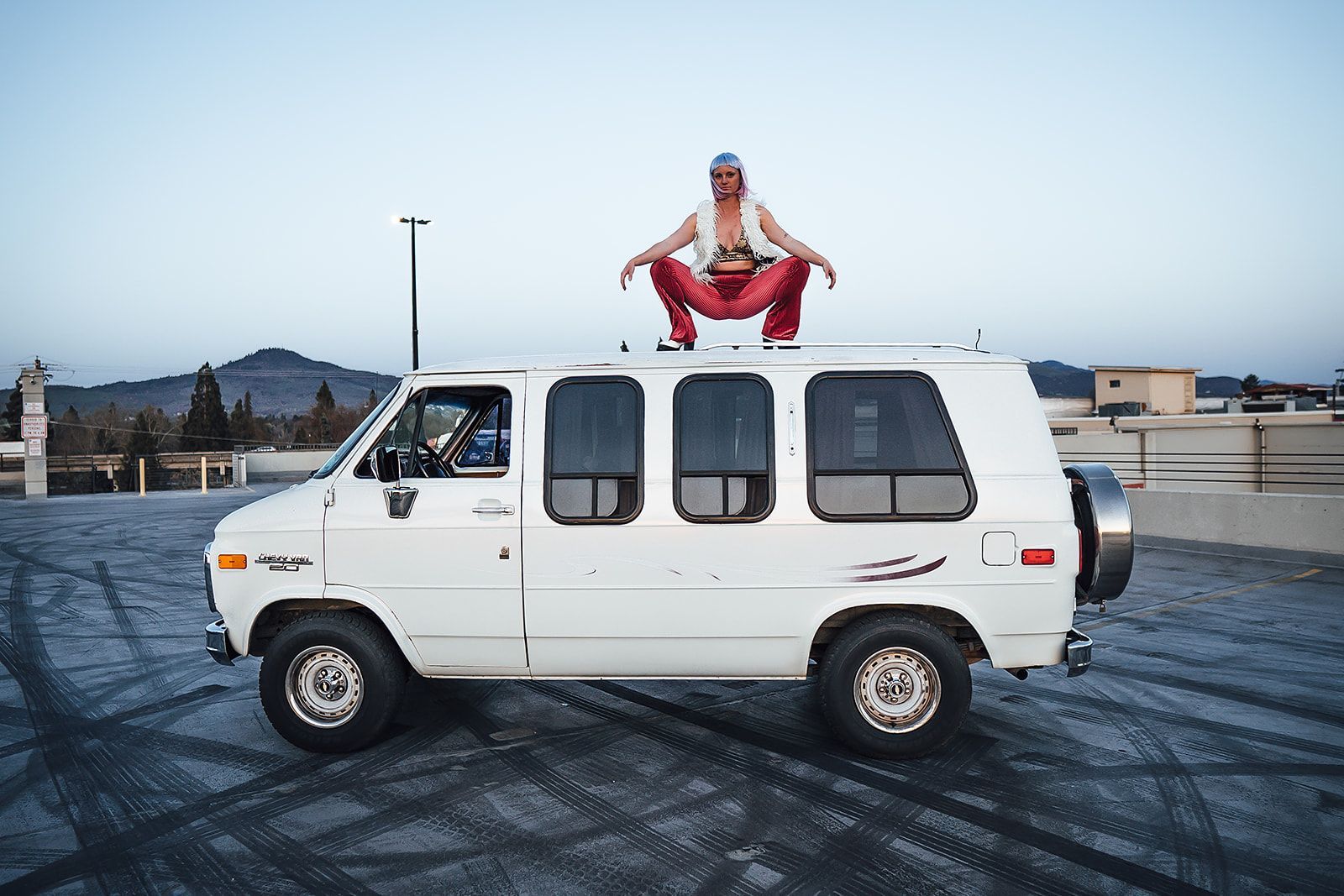A man is sitting on top of a white van in a parking lot.