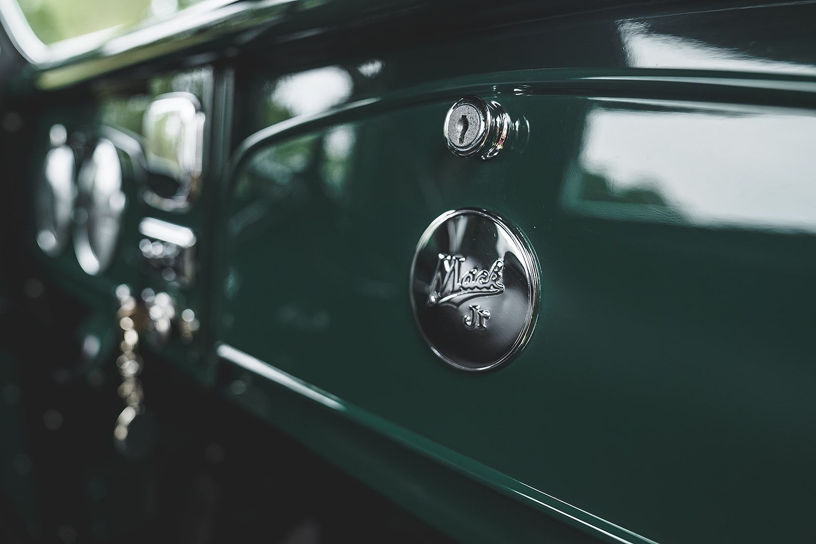 A close up of a green car with a silver emblem on the side.