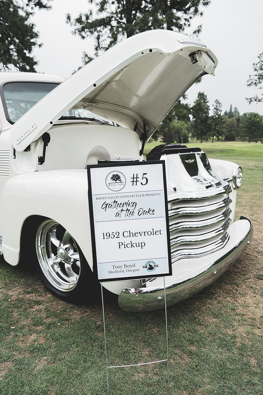 A white truck with the hood up is parked in a grassy field.