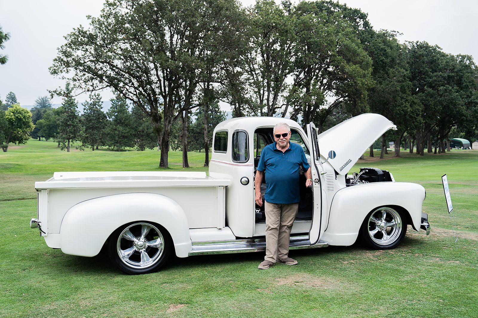 A man is standing next to a white truck with the hood open.