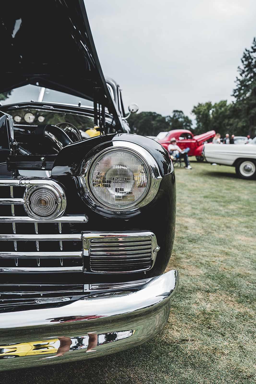 A close up of a black car with the hood up at a car show.