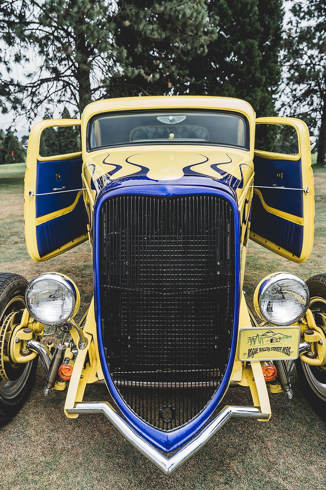 A yellow and blue car with its doors open is parked in a field.